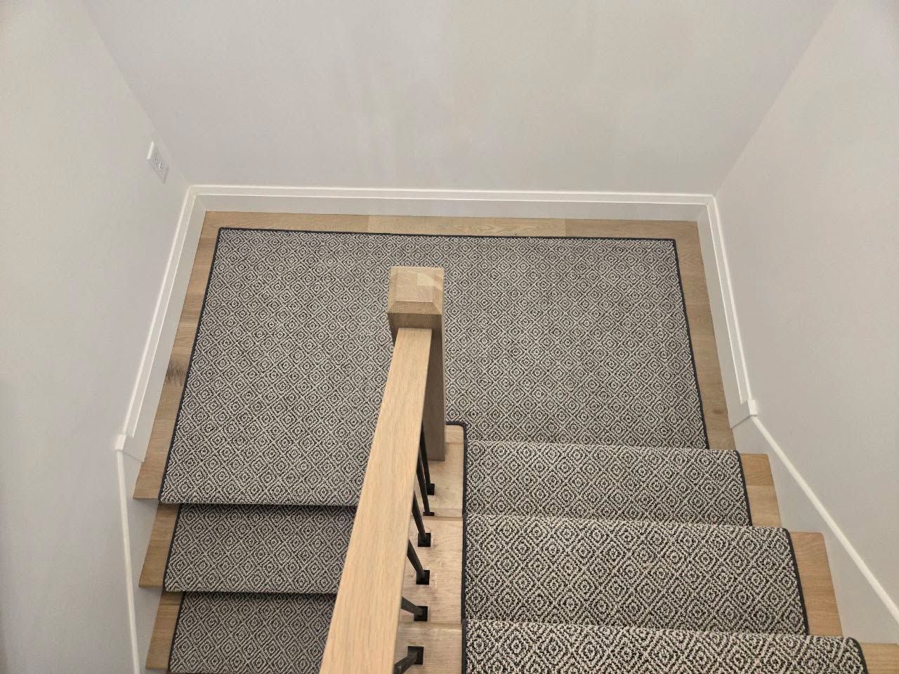 Staircase with gray geometric patterned carpet and maple wood border treads.
