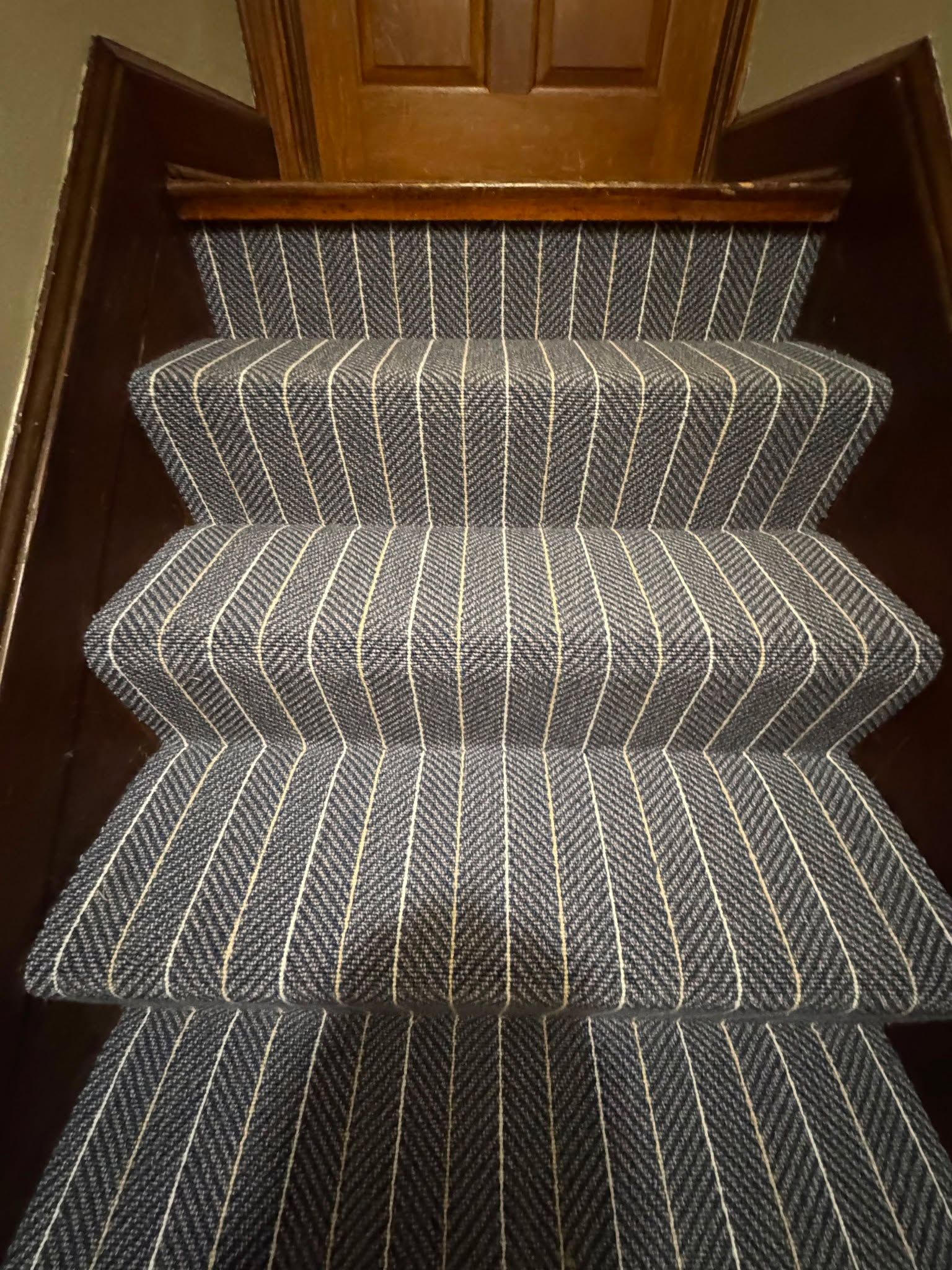 Staircase with chevron-patterned gray and white striped carpet and wooden handrails.
