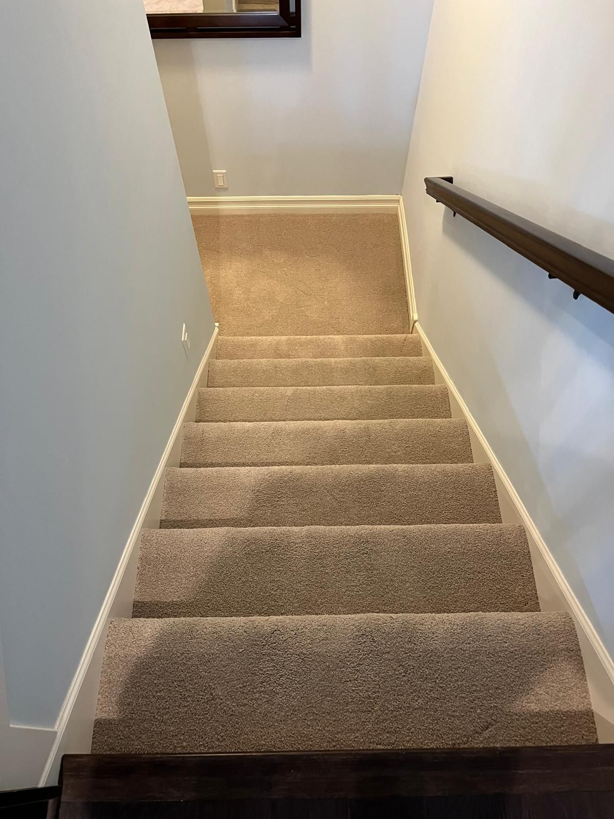 Beige carpet installed on staircase with white trim and dark wood handrail.