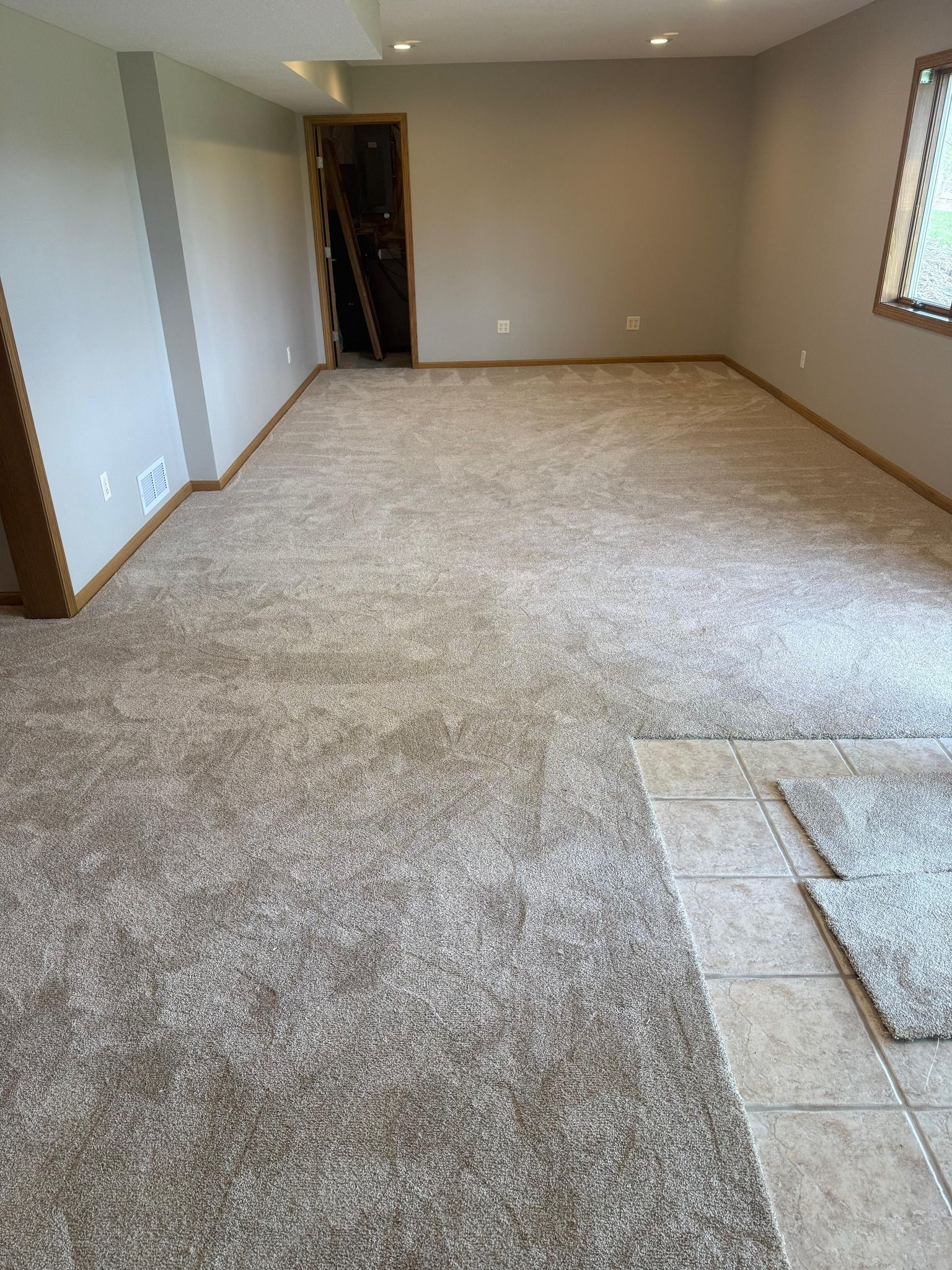 Newly installed light beige carpet in a basement room with wood trim and recessed ceiling lights.