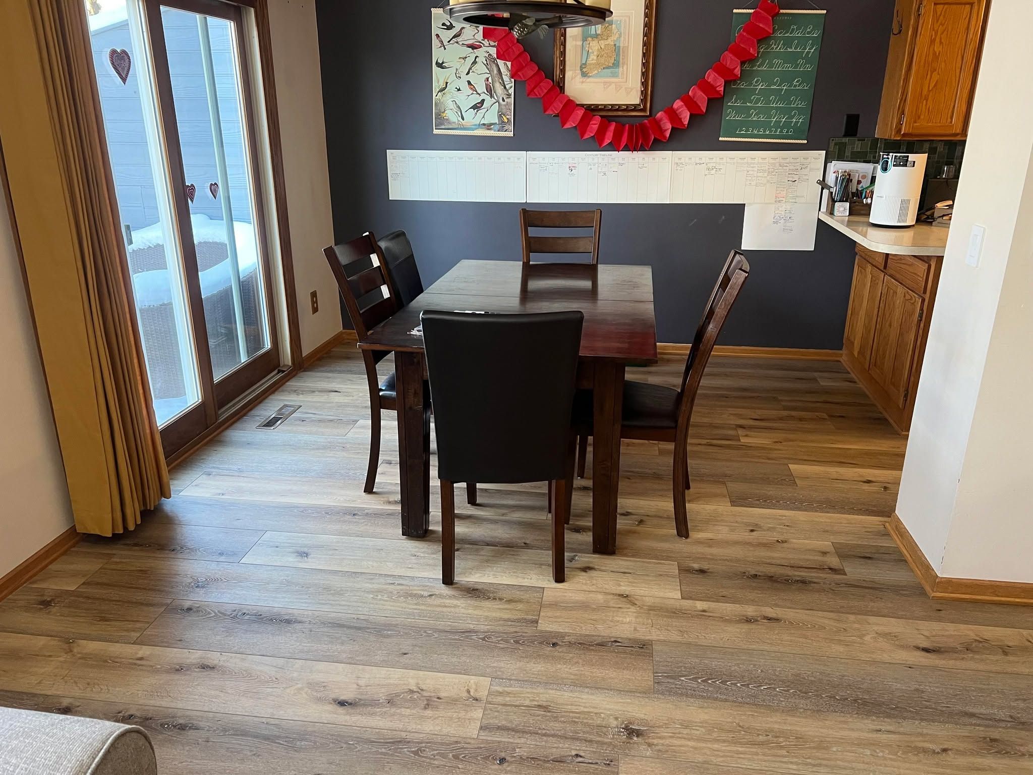 Kitchen and dining area with medium-toned wood-look LVP planks and wooden furniture.