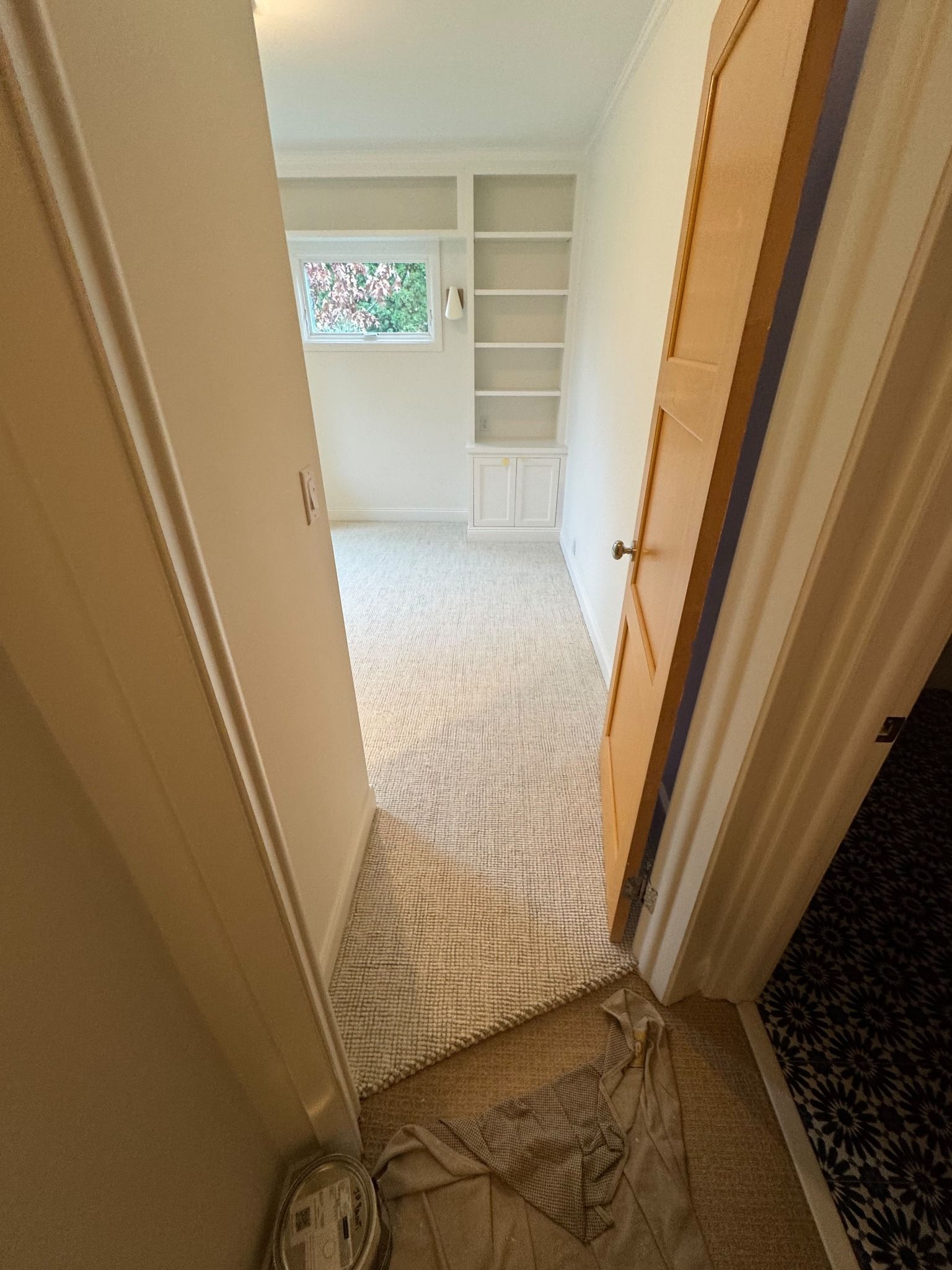 Light beige textured carpet installed in a hallway with white trim and built-in shelving visible at the end.