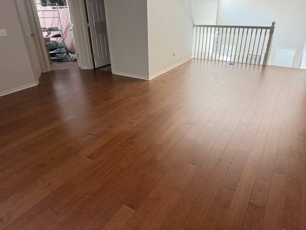 Medium brown hardwood plank flooring in a living room with a metal railing and open layout.