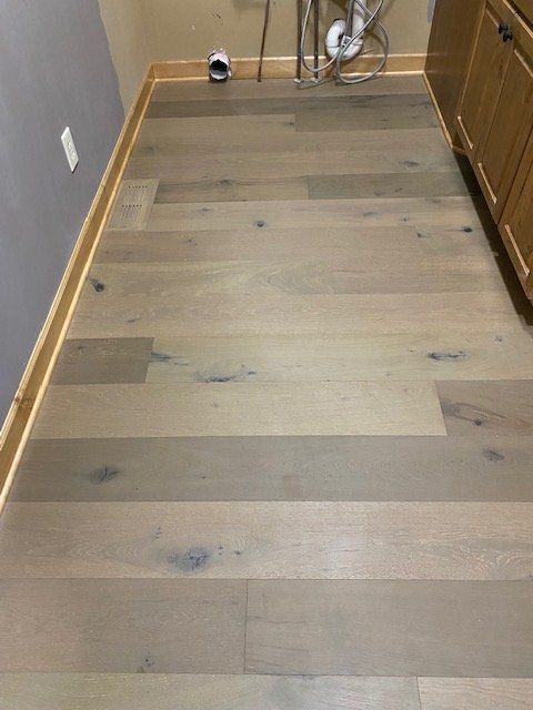 Light-colored hardwood plank flooring installed in a bathroom with visible grain and knots.