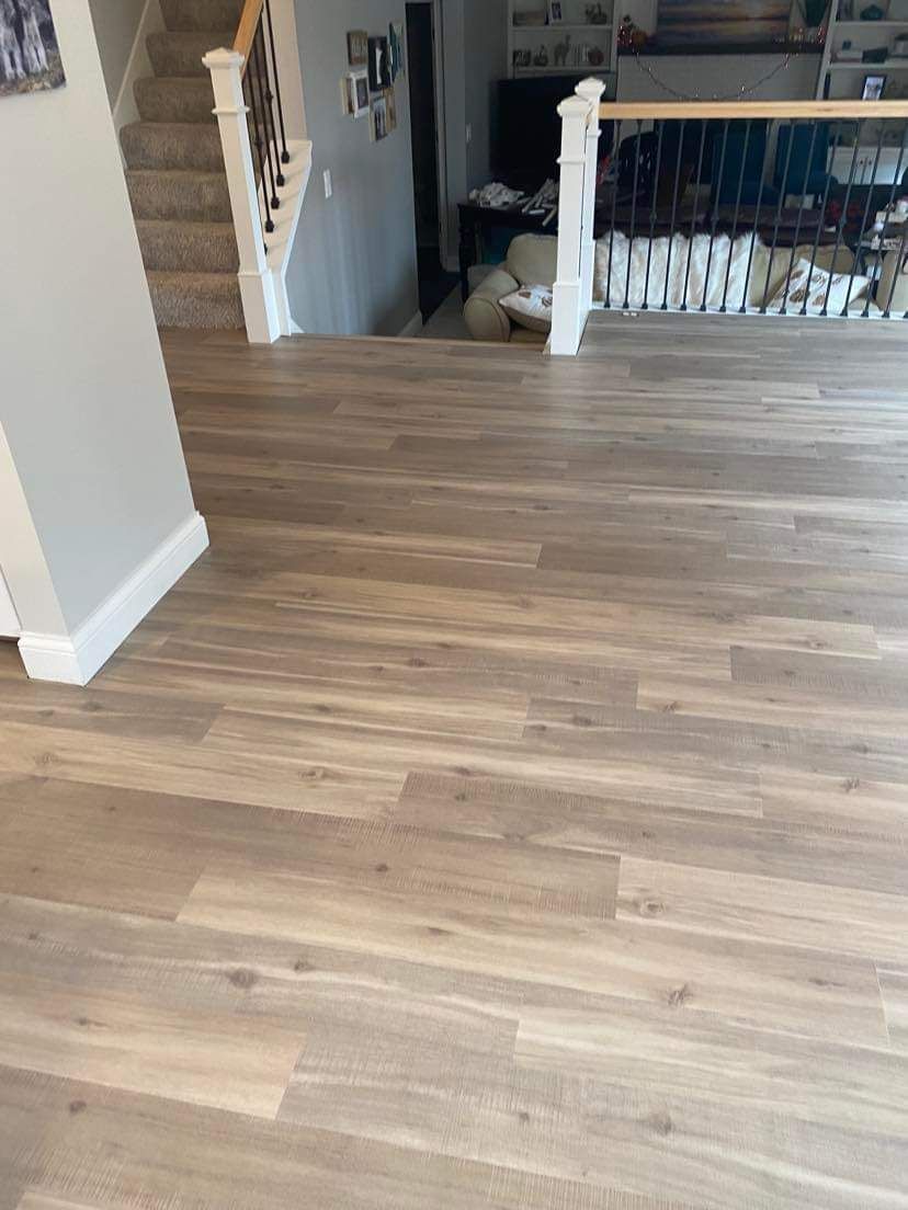 Light to medium brown wood-look LVP planks installed in a residential living area with white baseboards and staircase transition visible.