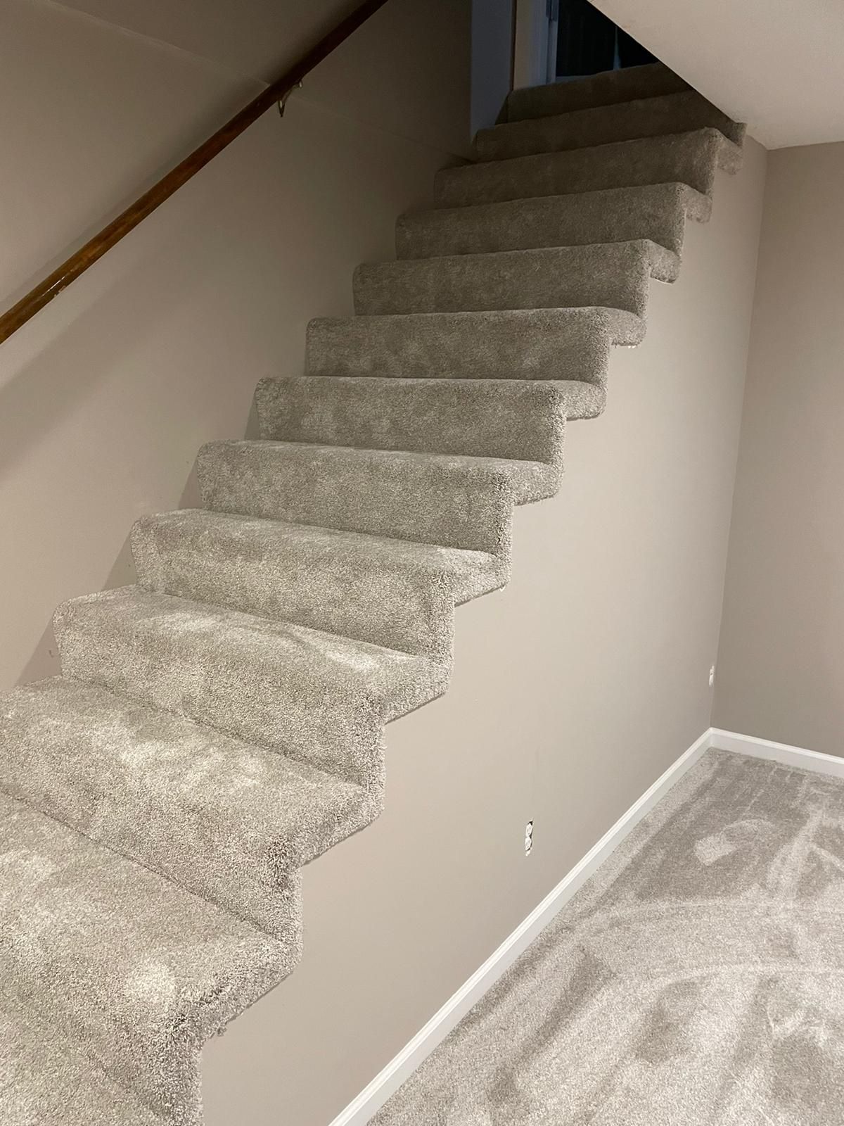 Newly installed light beige carpet on staircase and basement floor with white walls and wooden handrail.
