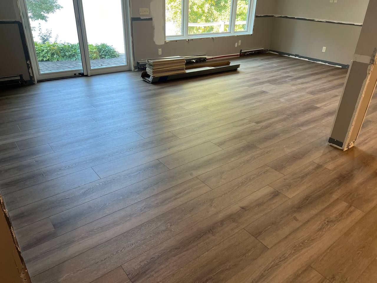 Luxury vinyl plank flooring installation in progress showing multi-toned planks in a living room with glass doors and windows.