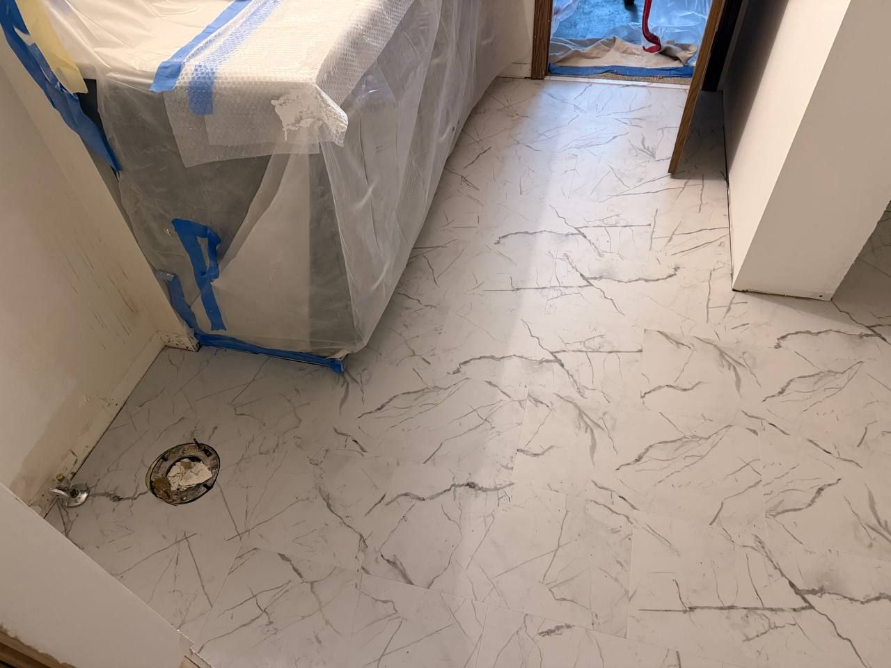 Newly installed light-colored LVP flooring with marble-like veining in a bedroom during construction.