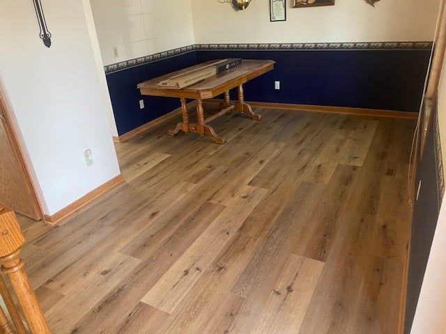 Basement recreation room with medium-tone wood-look LVP plank flooring installed throughout.