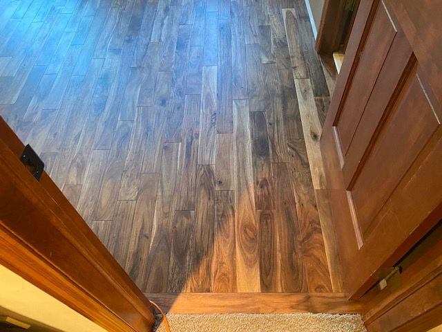 Herringbone pattern acacia hardwood flooring in entry with wood grain variation transitioning to carpet.