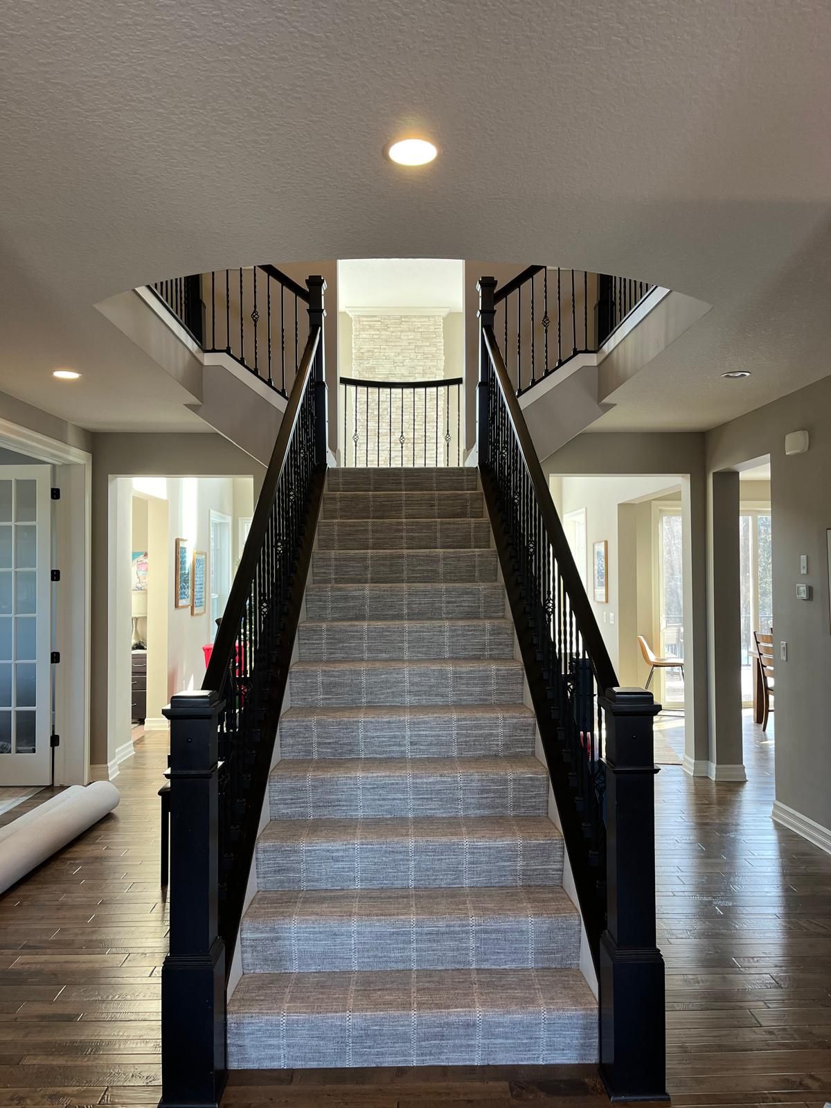 Carpeted staircase with geometric patterned runner in gray and brown tones between black railings.