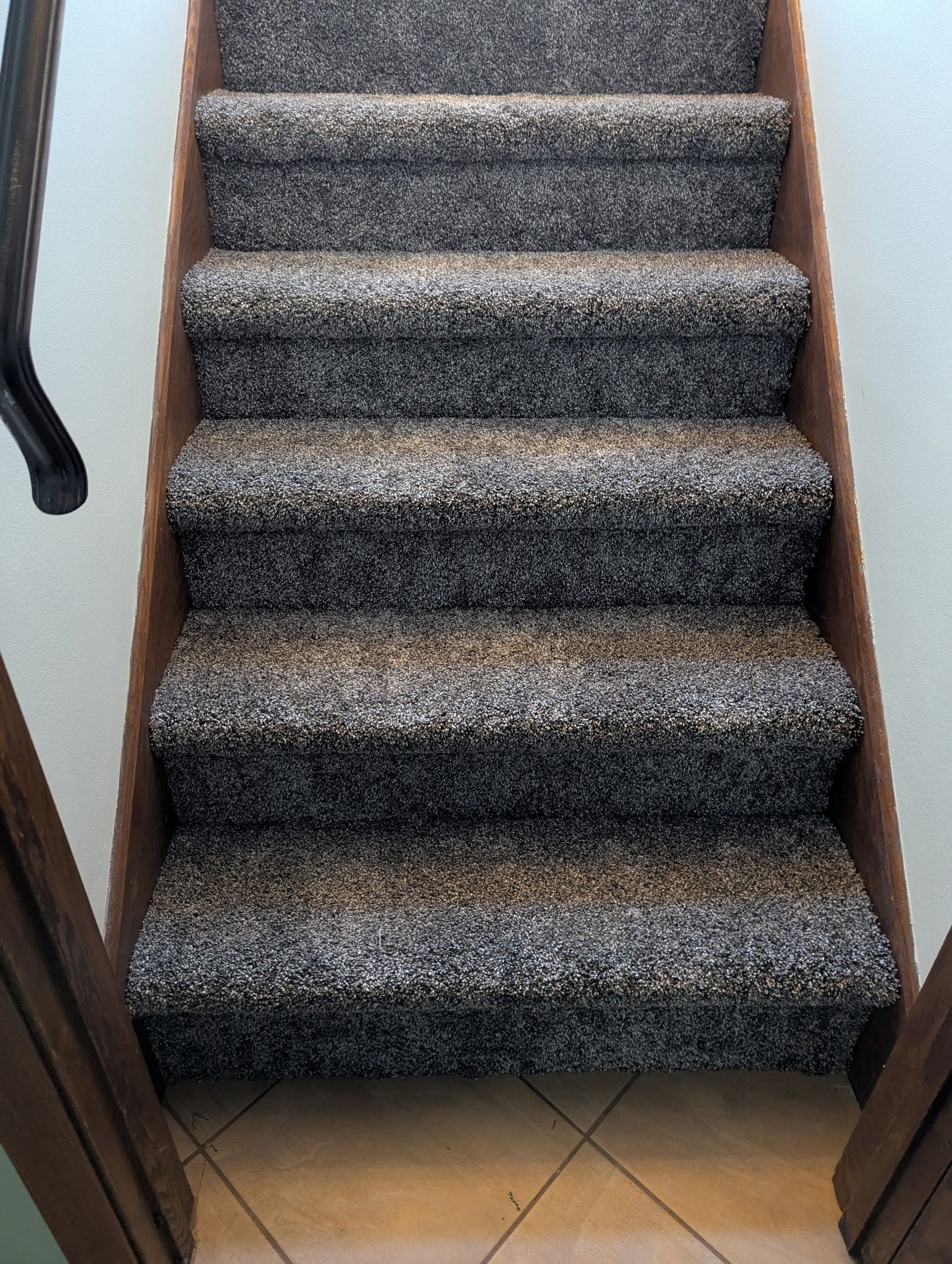 Gray carpet installed on interior staircase with wood sides and black handrail.