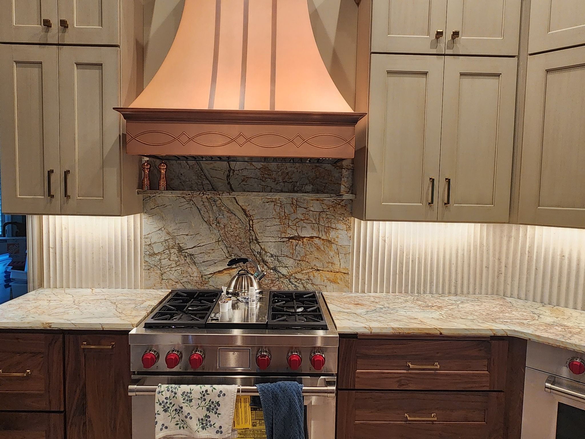 Natural stone slab backsplash behind a range with a copper hood