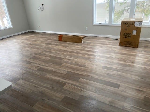 Newly installed light to medium brown plank LVP flooring in a spacious living room with large windows.