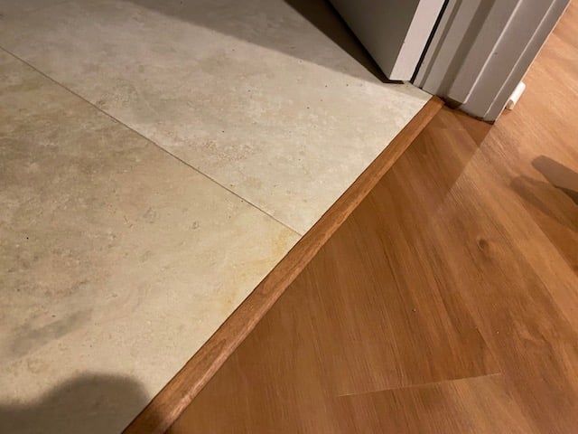 LVP flooring transitioning from wooden plank in kitchen to concrete floor at appliance area.