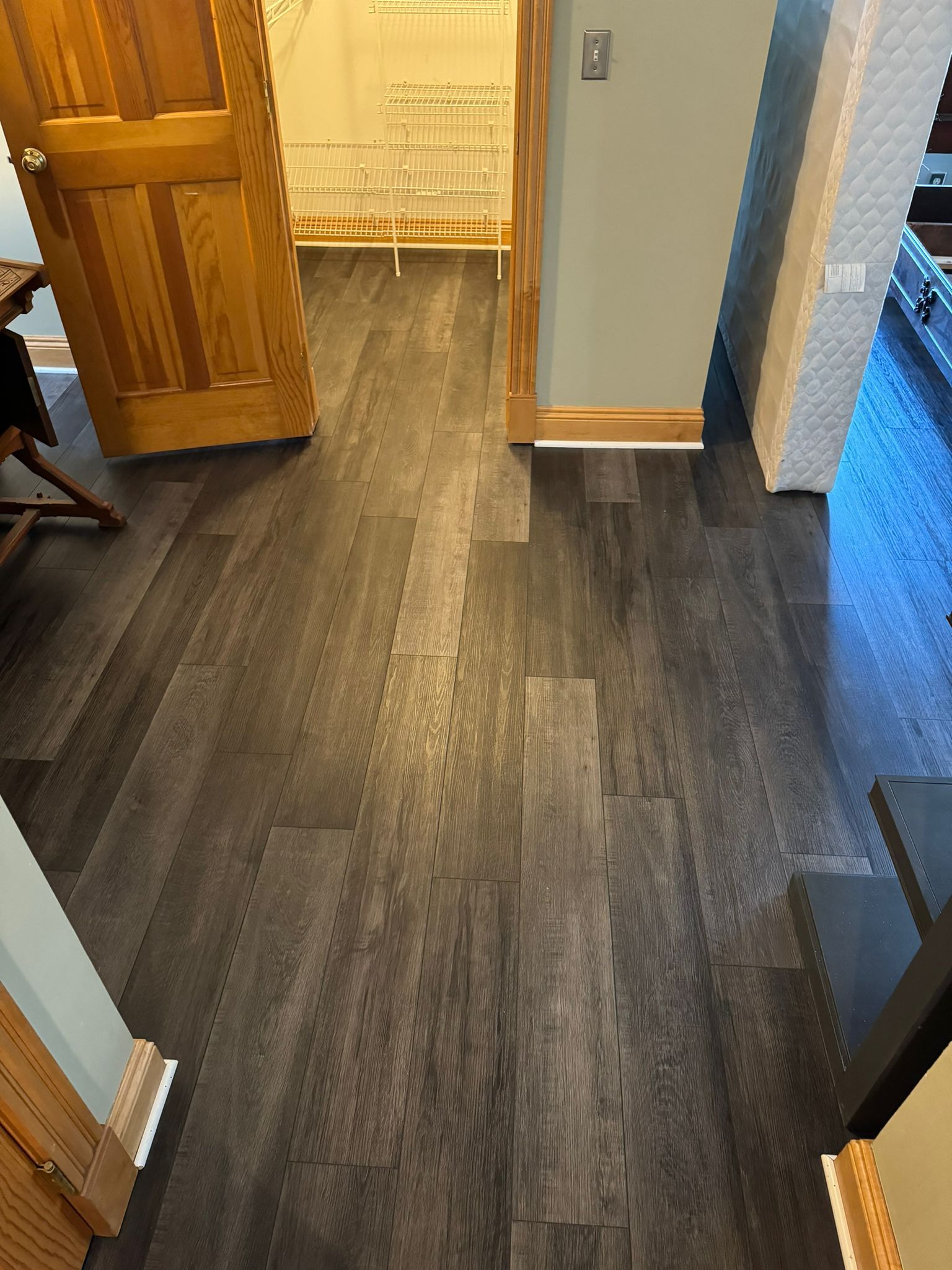 Dark gray and brown wood-look LVP planks installed in a hallway with wooden door frames and transition strips at doorways.