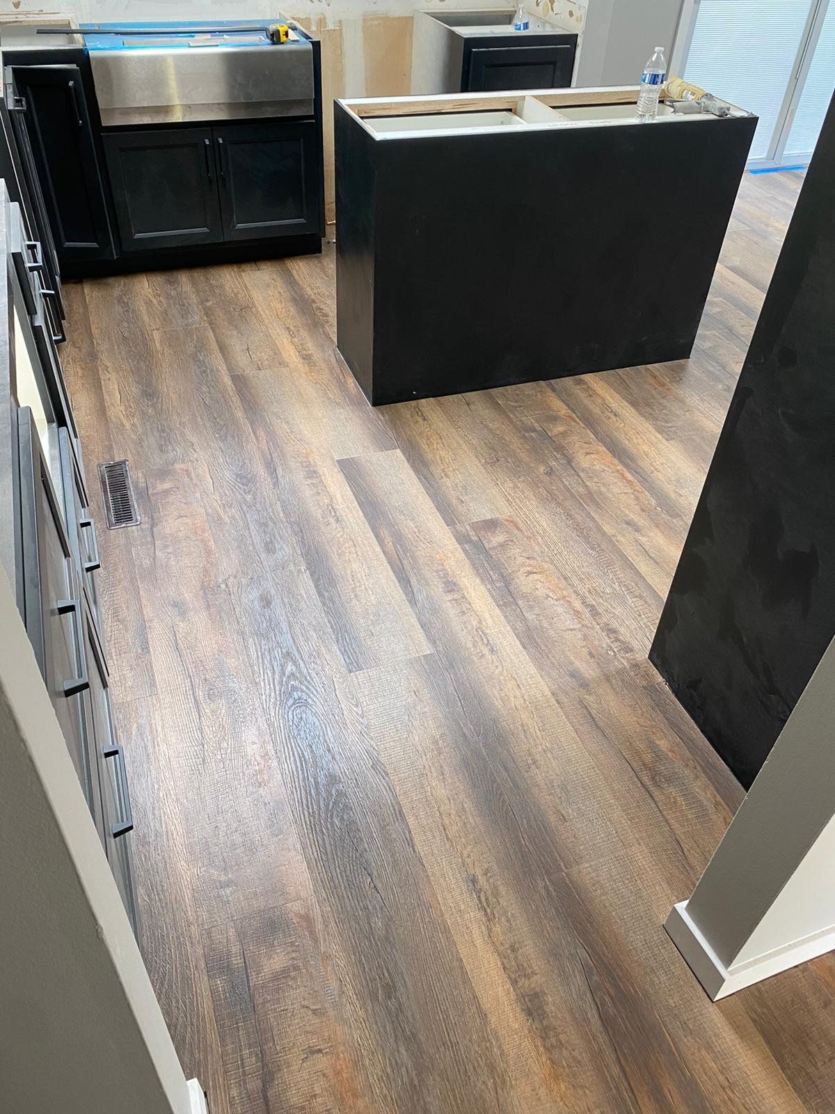 LVP plank flooring in medium brown tones installed in a kitchen with black cabinetry and island during remodel.