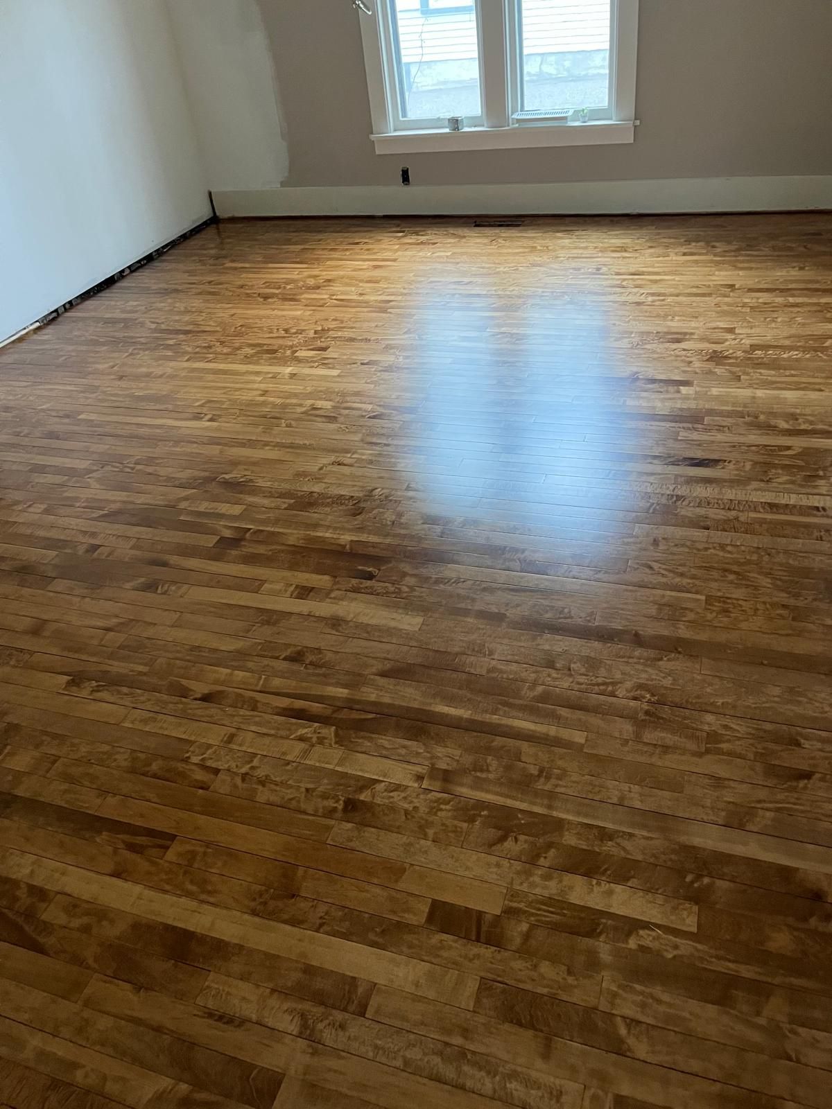 Newly refinished hardwood plank flooring in a bedroom with window.