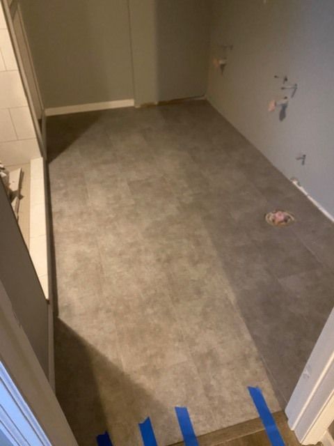 Bathroom with gray and tan plank LVP flooring installation in progress with protective tape applied.
