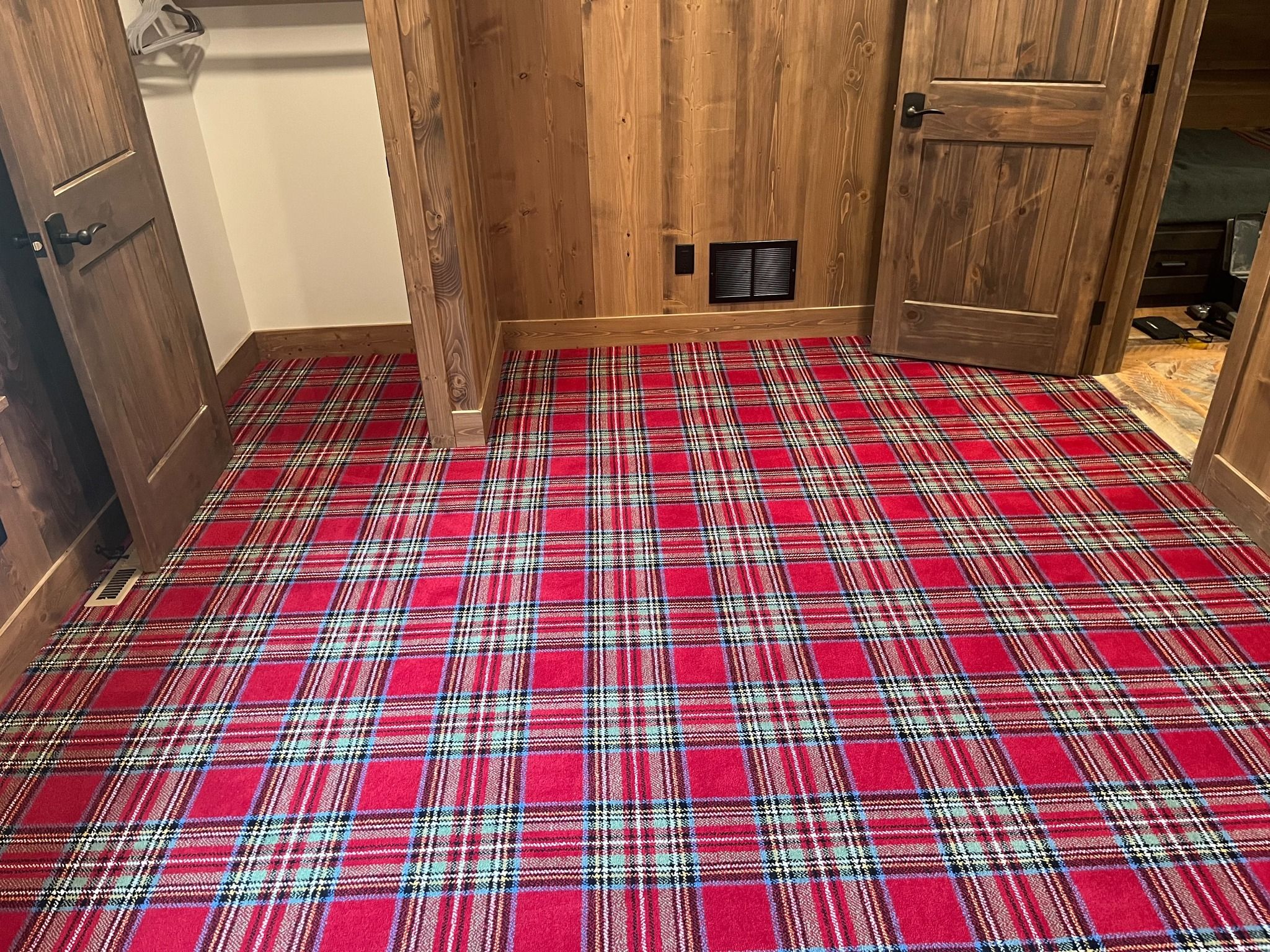 Red and white plaid patterned carpet installed in a bedroom with wood doors and paneled walls.