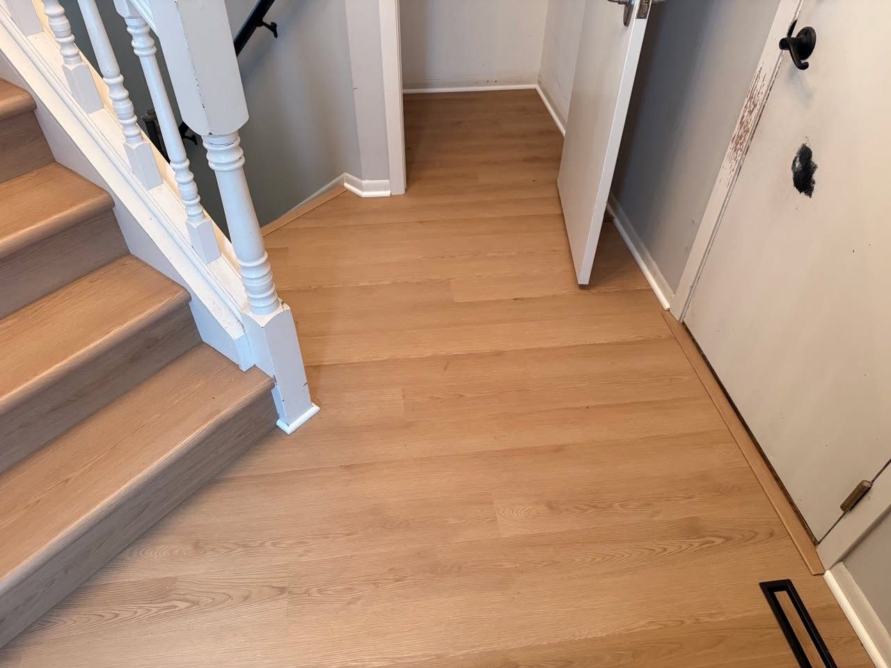 LVP hallway with white oak appearance and matching white baseboards leading to stairs.