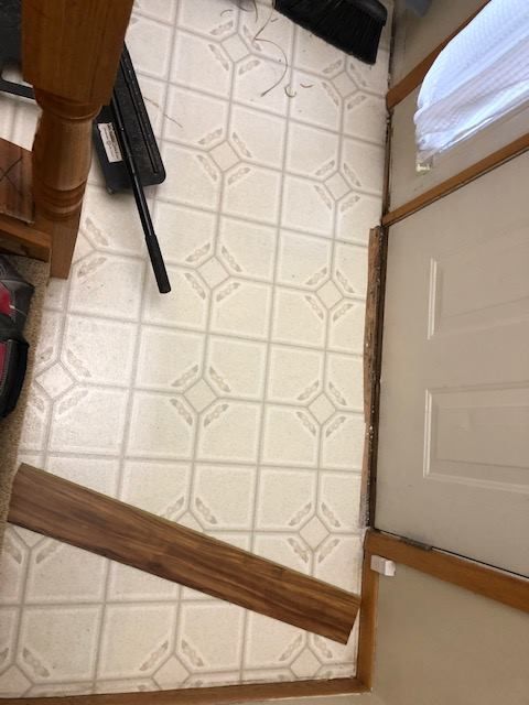 Cream and beige hexagonal patterned LVP flooring installed in an entryway with wood transition trim and wooden frame borders.