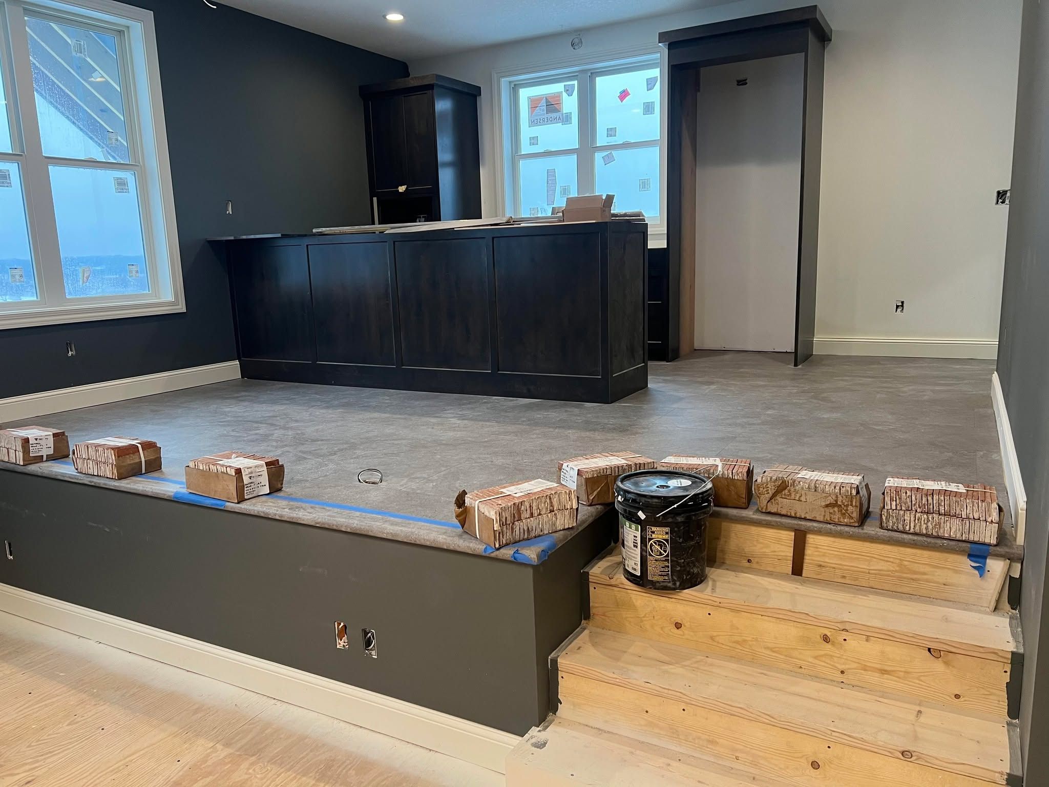 LVP flooring installation in progress in a commercial-style interior space with black cabinetry and windows.