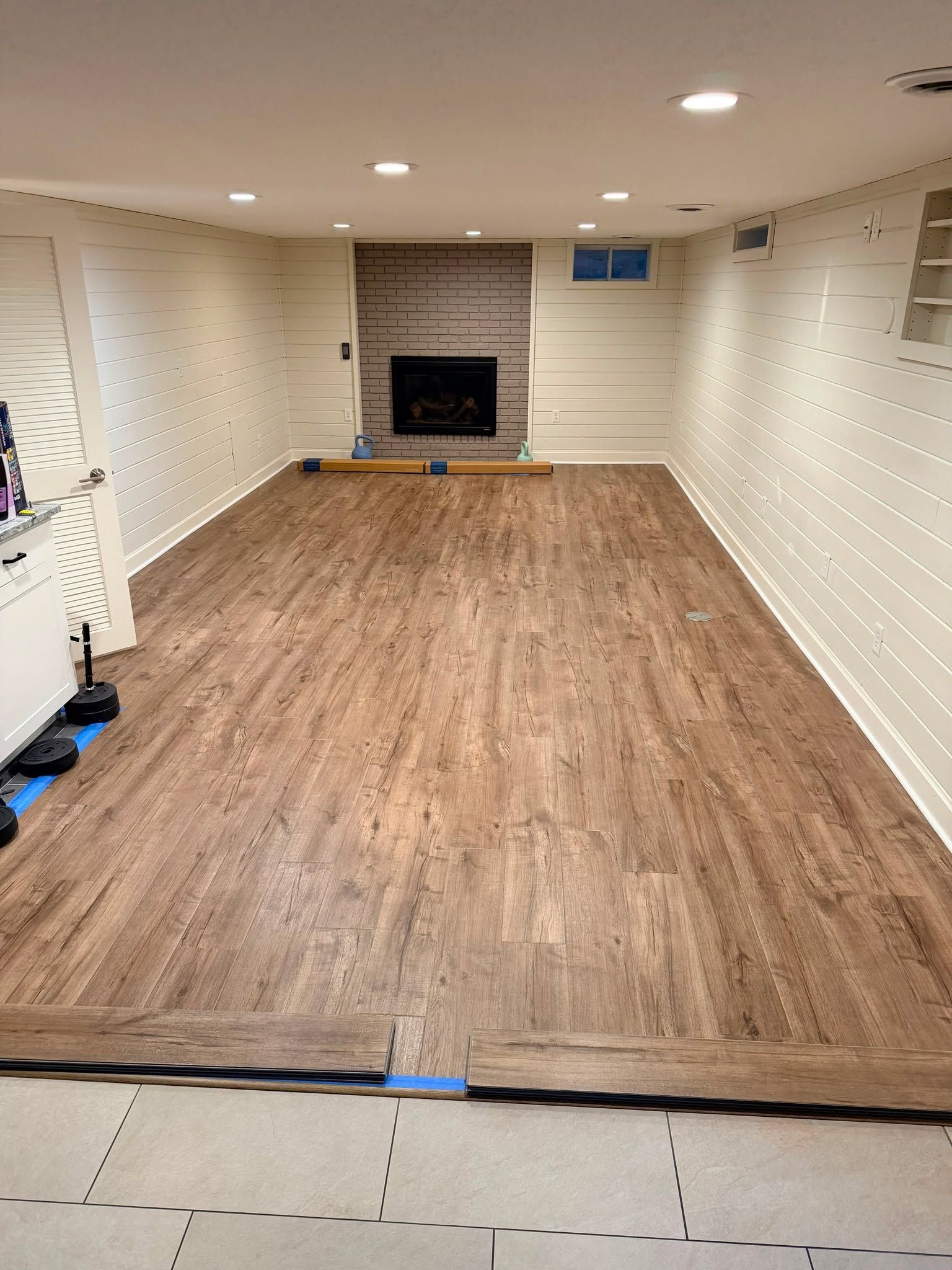 Newly installed medium-toned wood-look LVP planks in a basement with fireplace and recessed lighting.