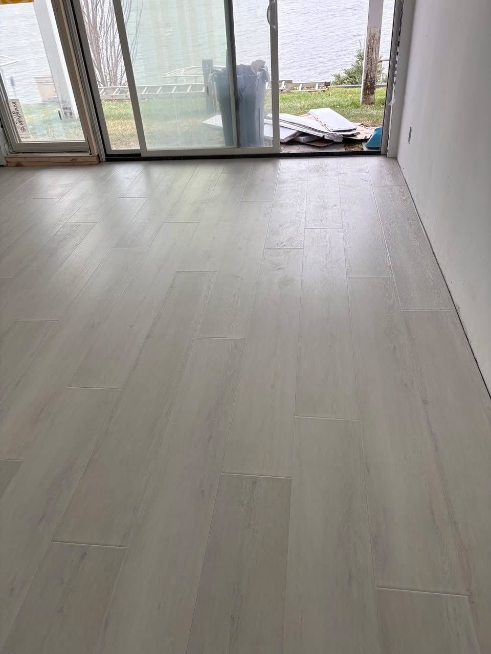 Light gray luxury vinyl plank flooring installed in a room with sliding glass doors overlooking water.