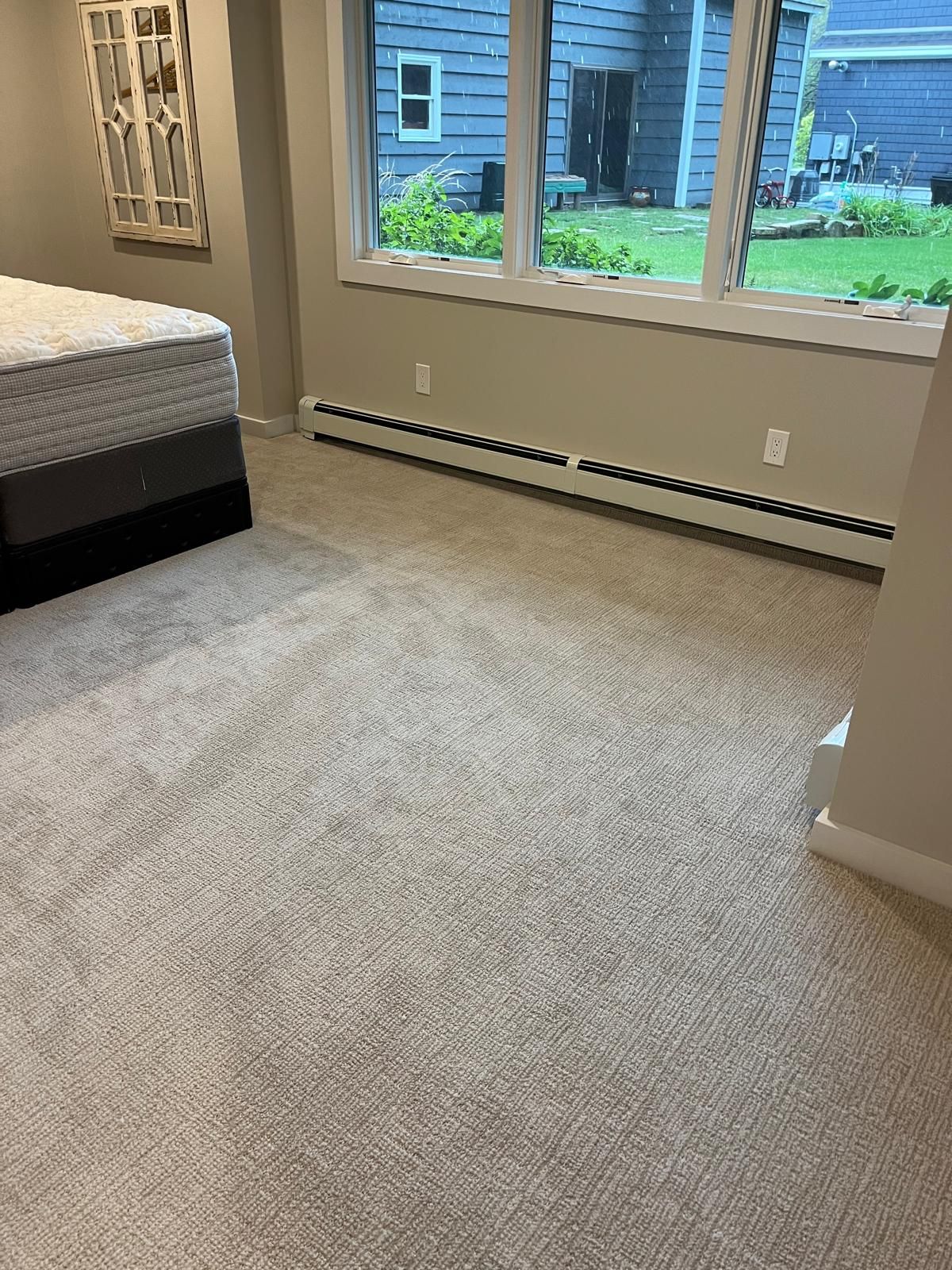Newly installed light beige carpet in a bedroom with large windows overlooking a backyard.