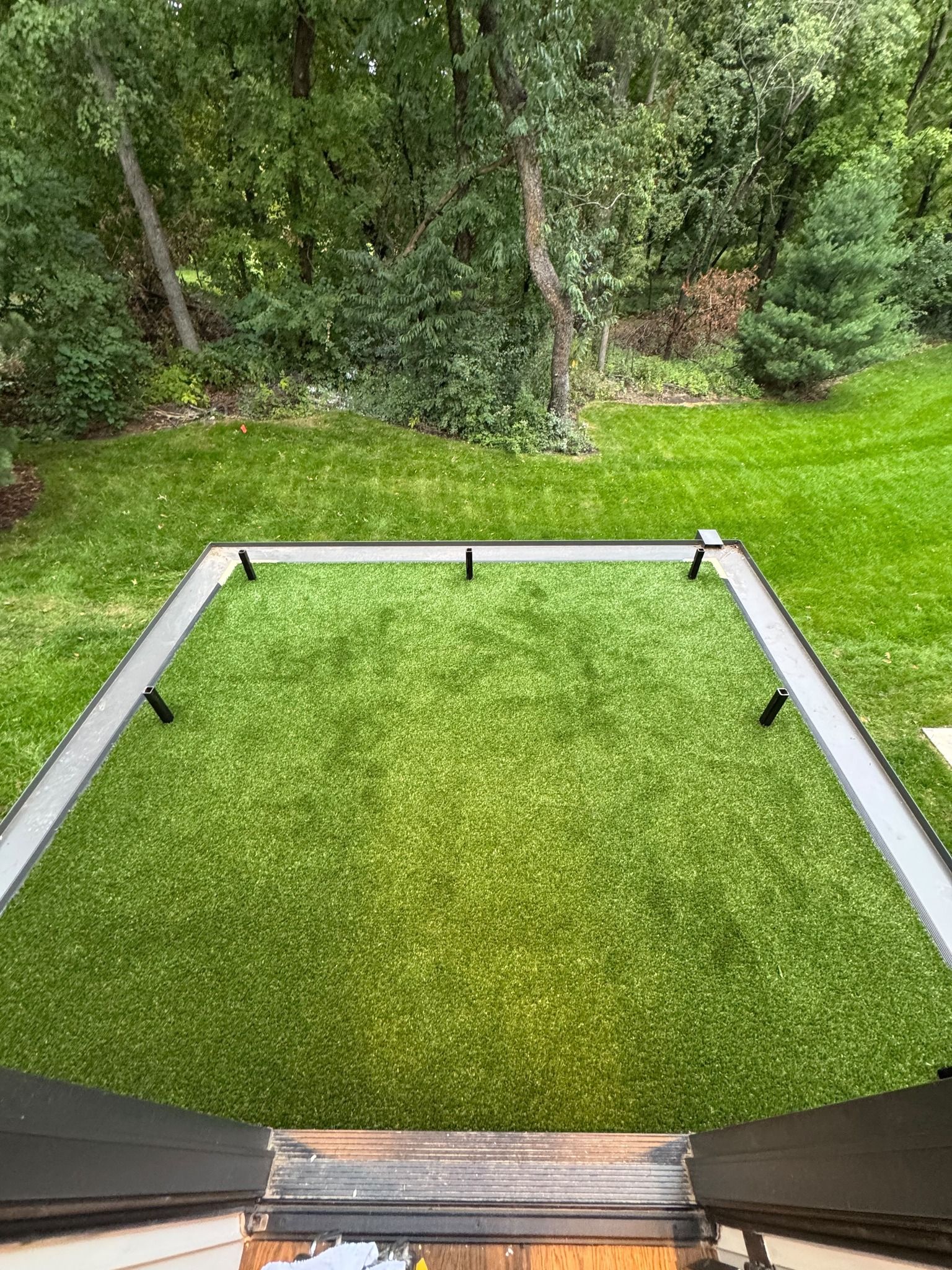 Artificial turf carpet installation in outdoor yard space with metal border edging and trees in background.
