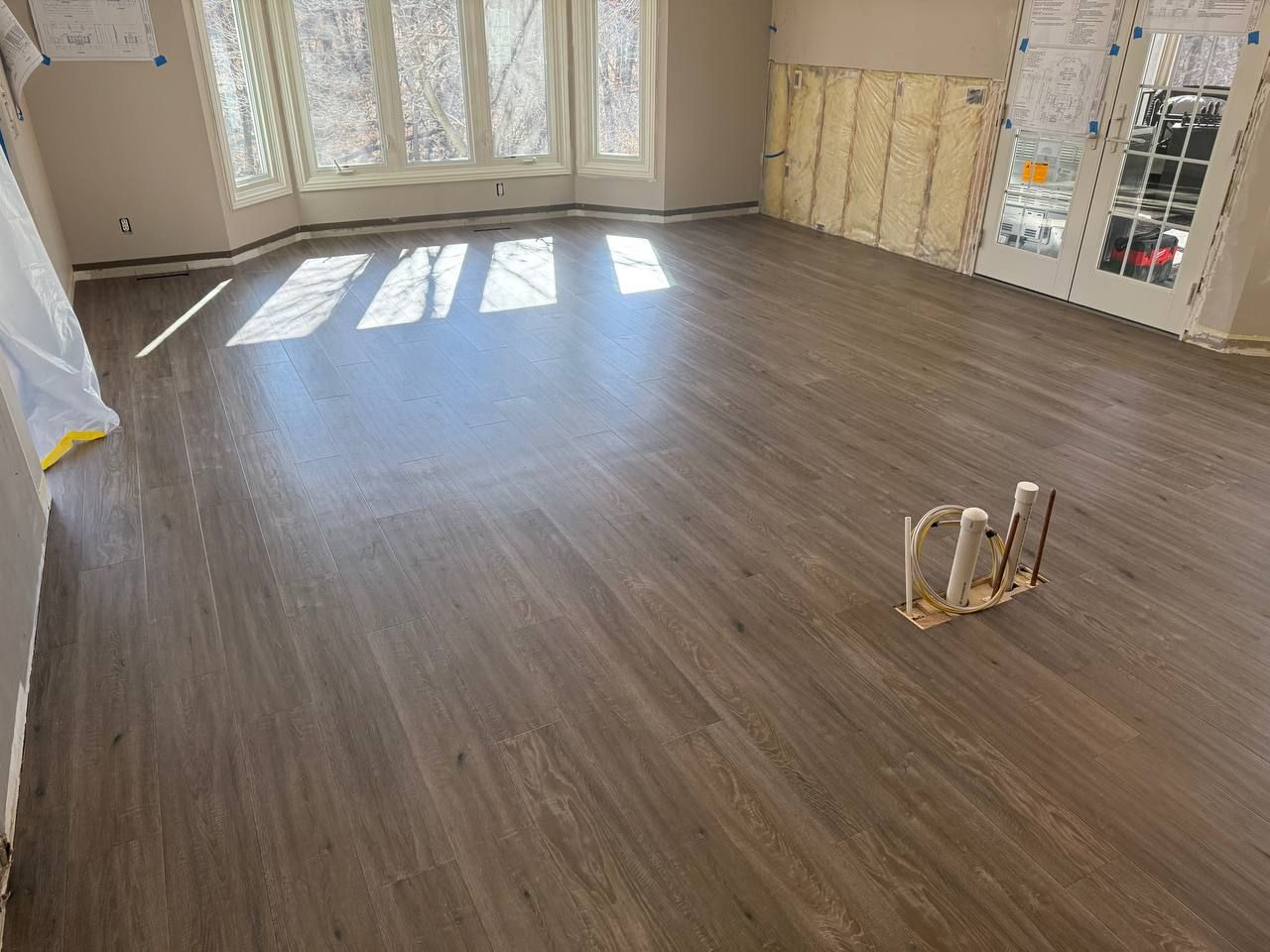 Newly installed medium-brown plank LVP flooring in a living room with large windows.