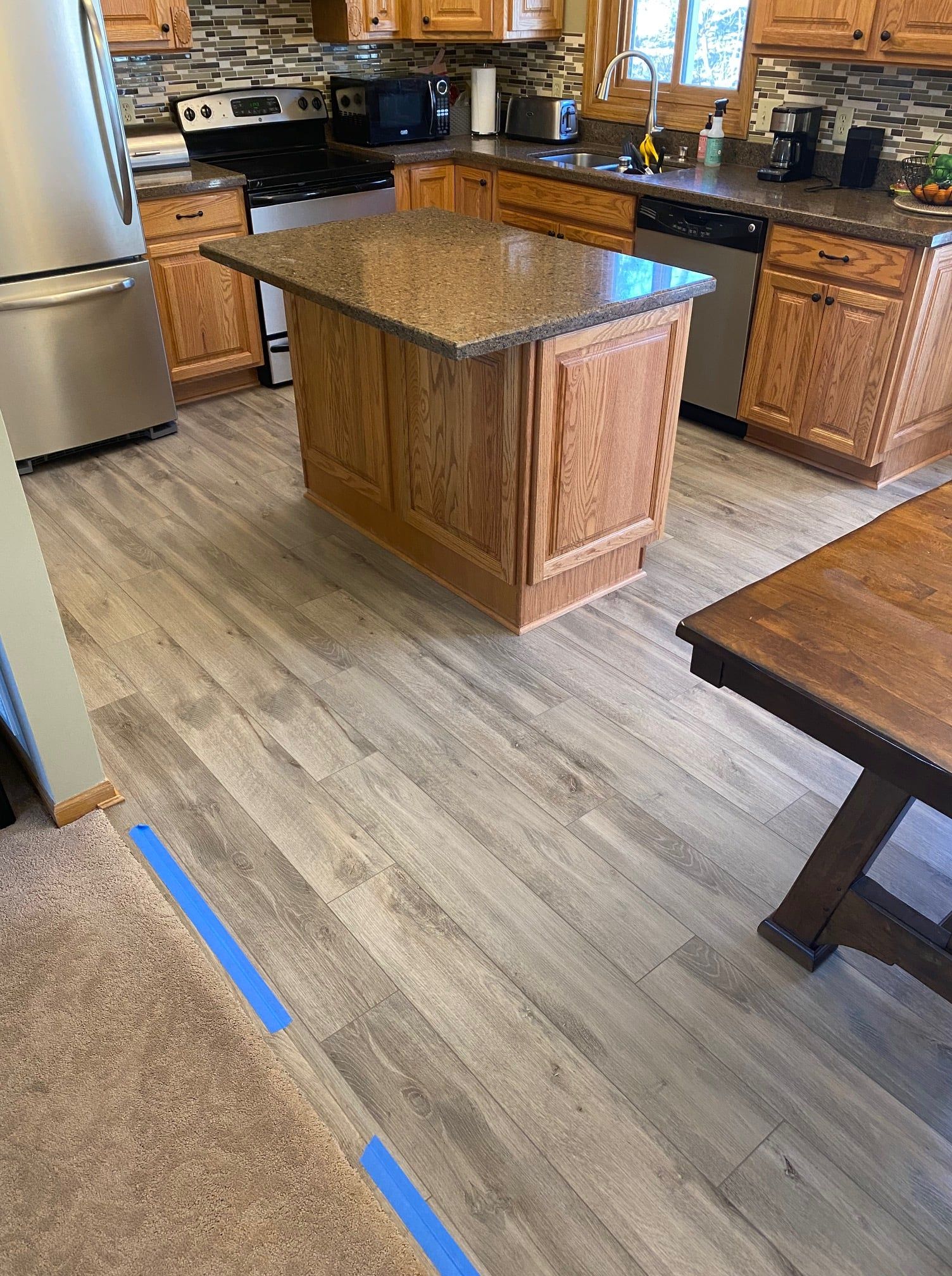 Kitchen with gray wood-look LVP flooring, wood cabinetry, island, and granite countertops.