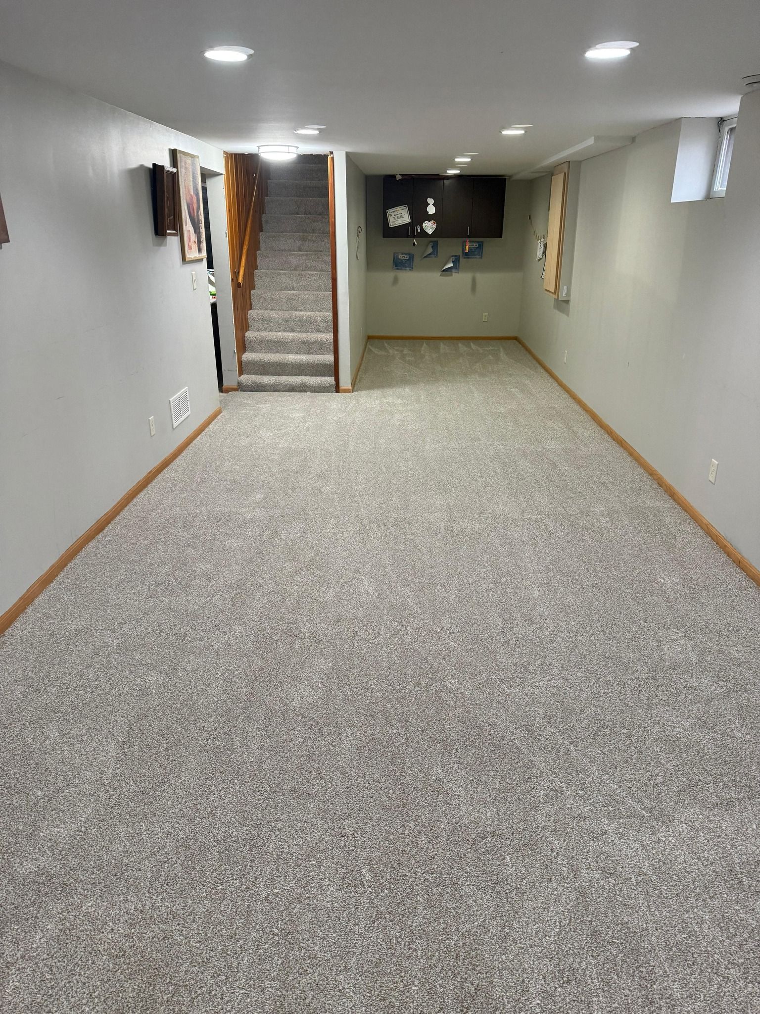 Newly installed light beige carpet in a basement room with wood baseboards and recessed ceiling lights.