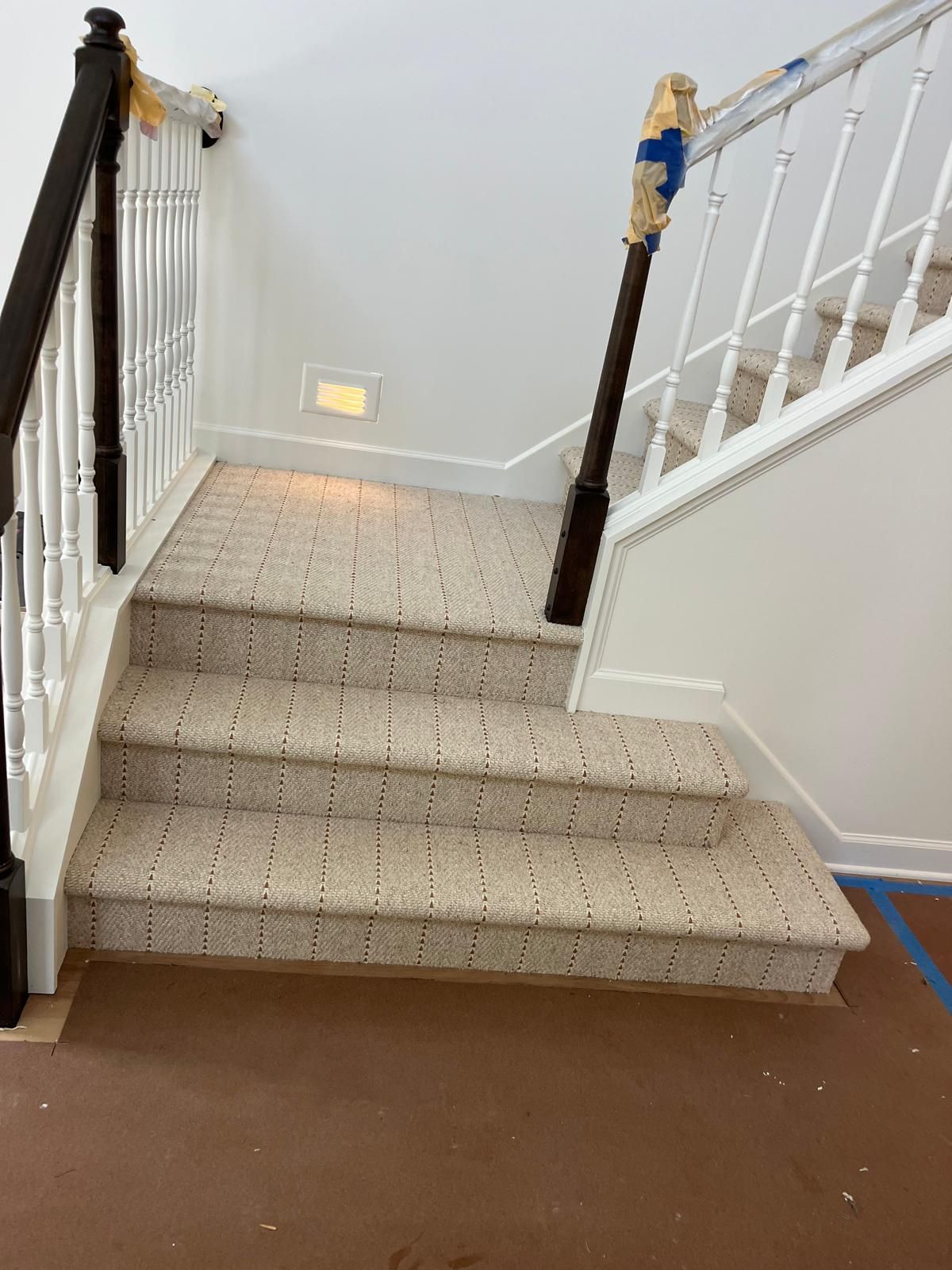 Beige patterned carpet installed on interior staircase with white balusters and dark wood handrails.