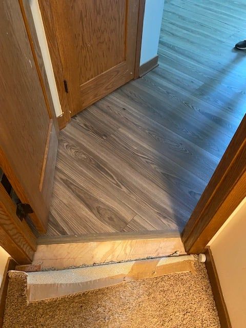 Gray and brown plank LVP flooring installed in a hallway with transition strip visible at entry point.