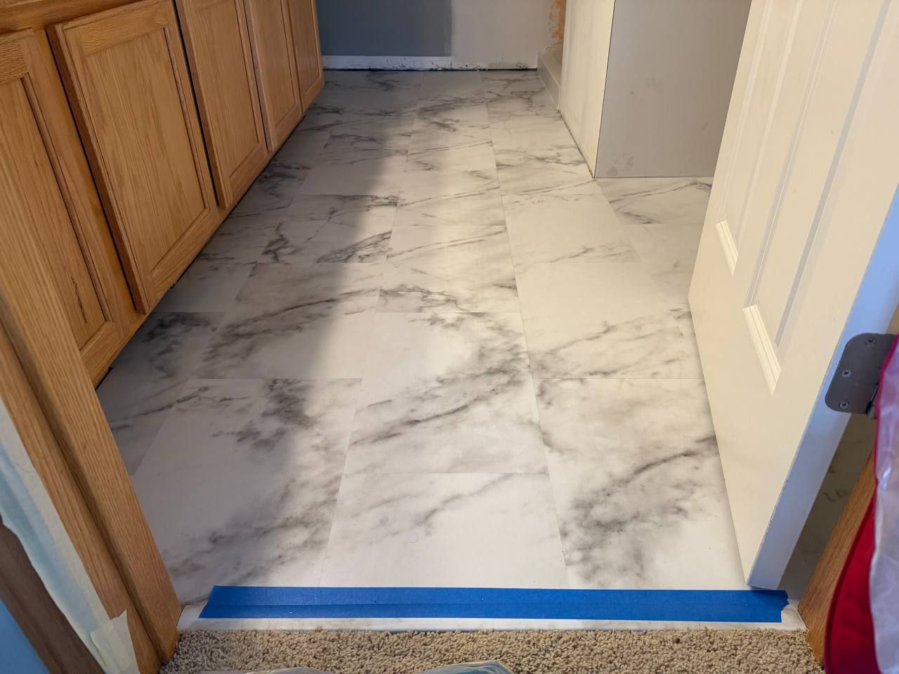Light-colored marble-look LVP planks installed in a kitchen with cream cabinets and hallway entry.