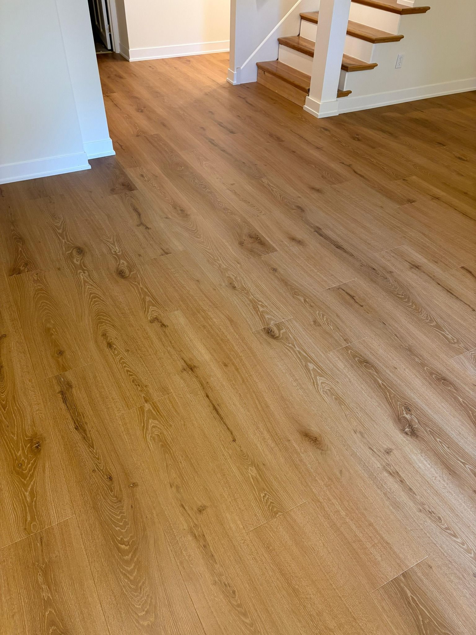 Light tan and brown plank LVP flooring installed in an entryway leading to stairs with white walls and trim.