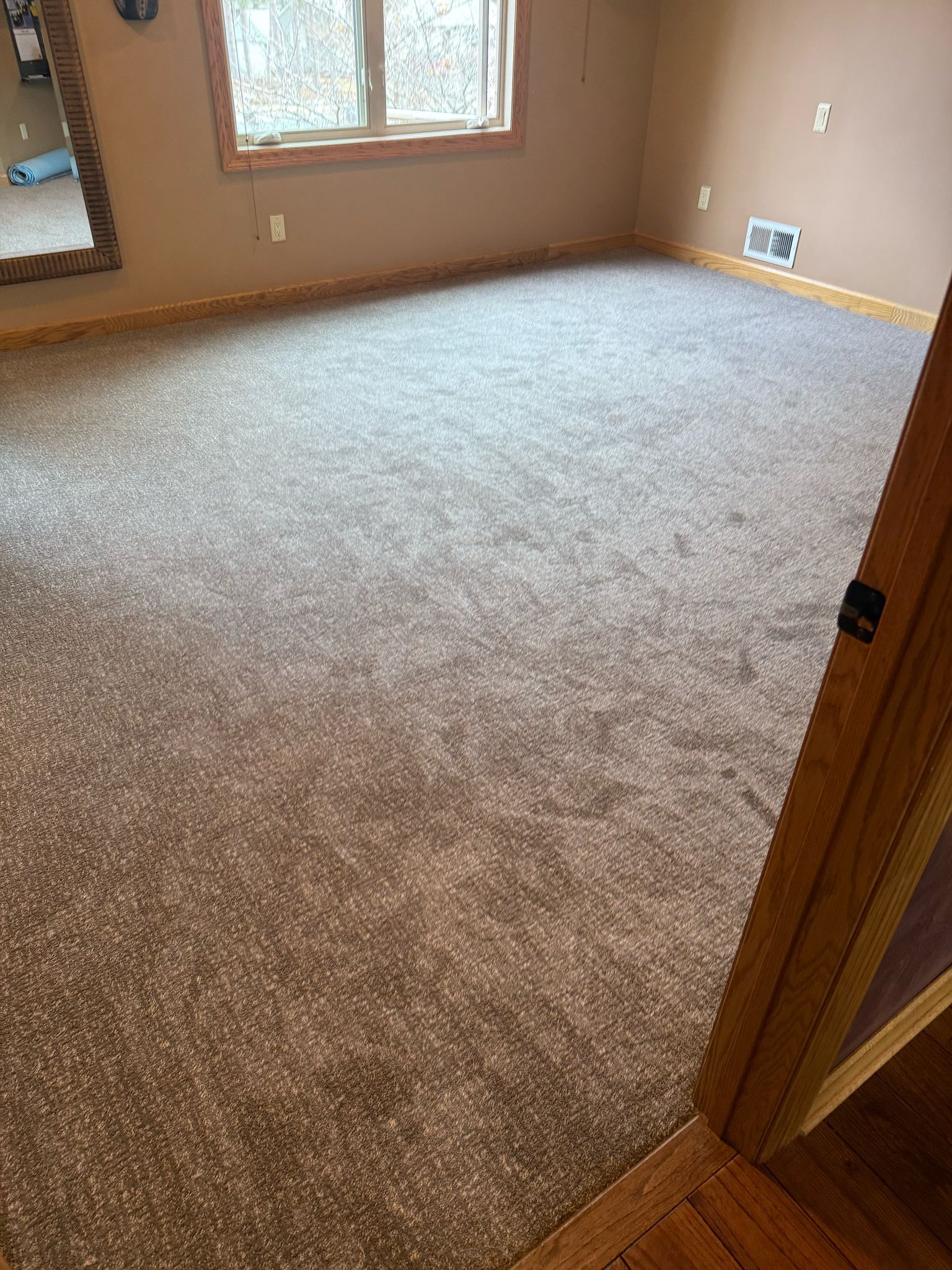 Light beige and gray textured carpet installed in a bedroom with wood trim and baseboard molding.