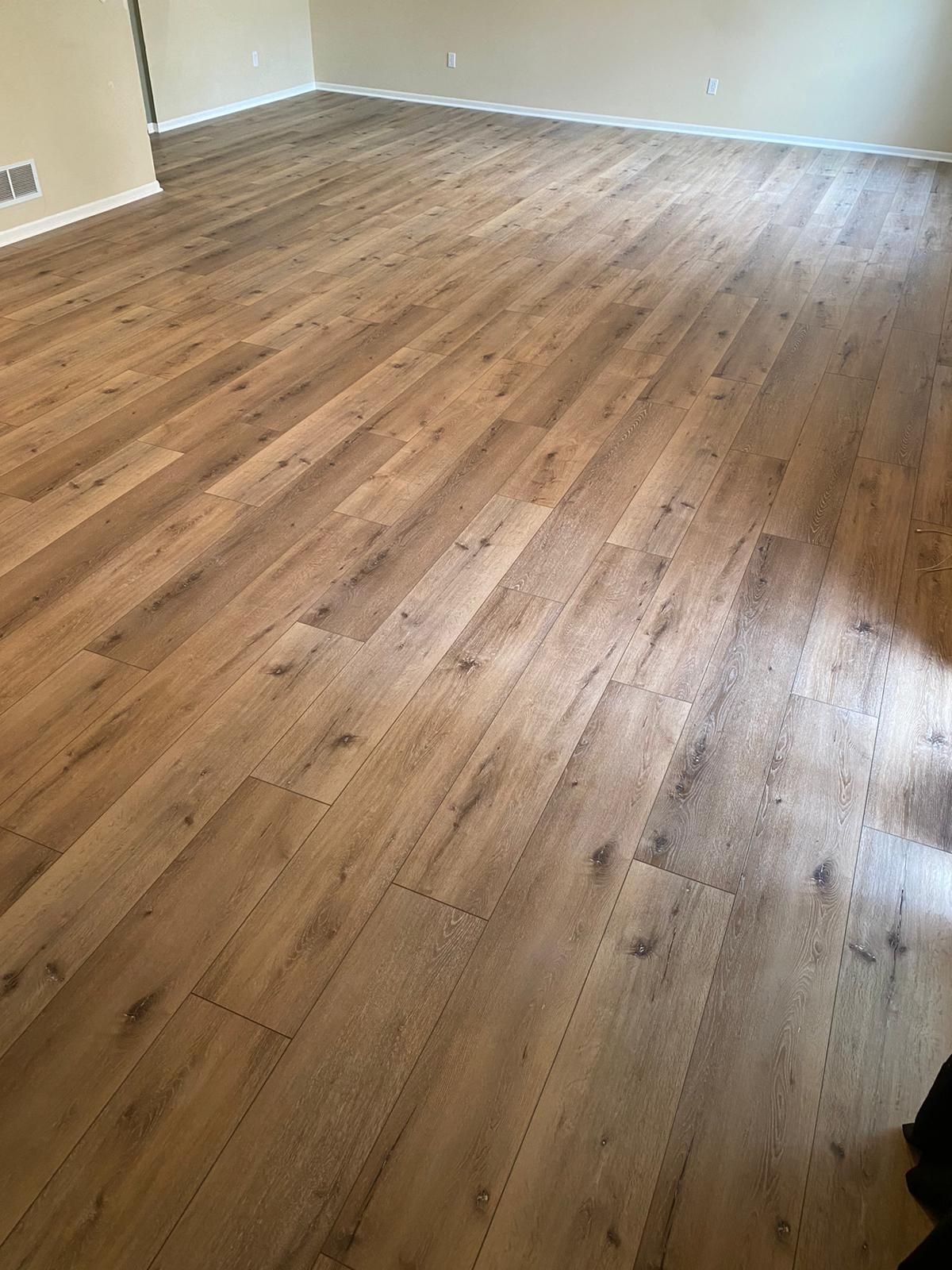Empty living room with medium brown plank LVP flooring installed throughout.