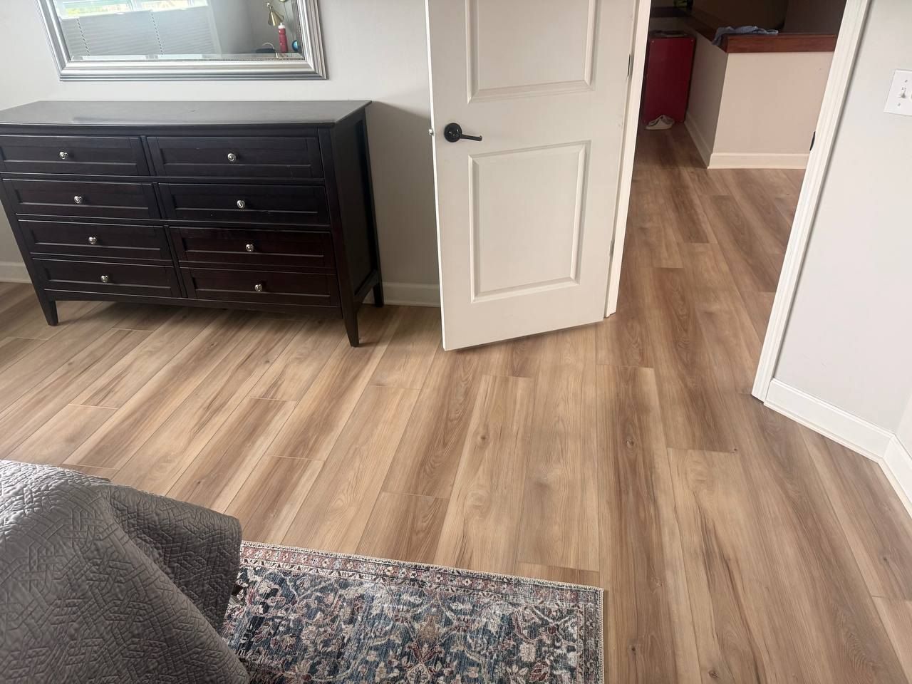 Bedroom with medium brown wood-look LVP planks installed throughout, with dark dresser and white closet door visible.