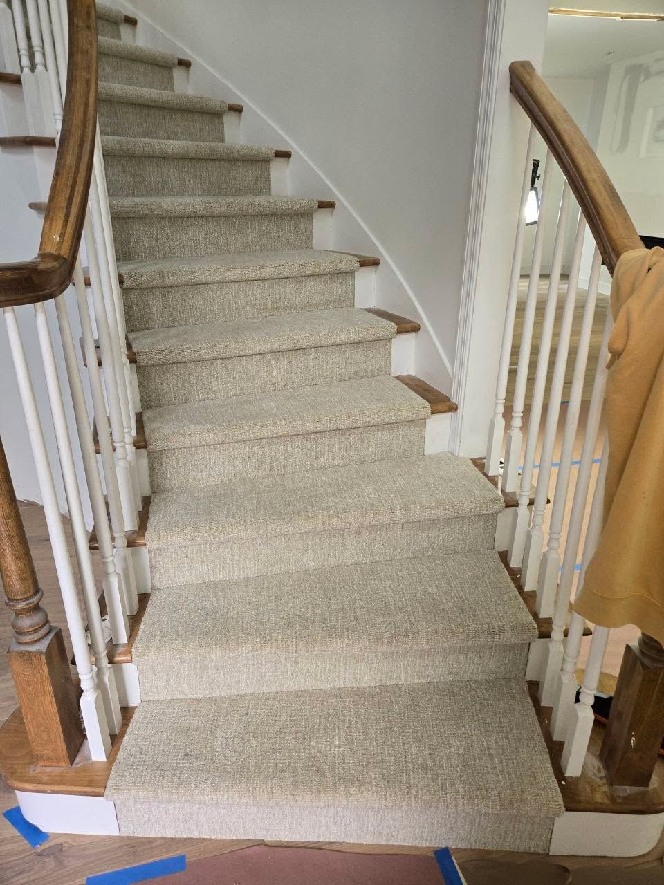 Beige wool carpet installed on staircase with wood nosing and white railings.