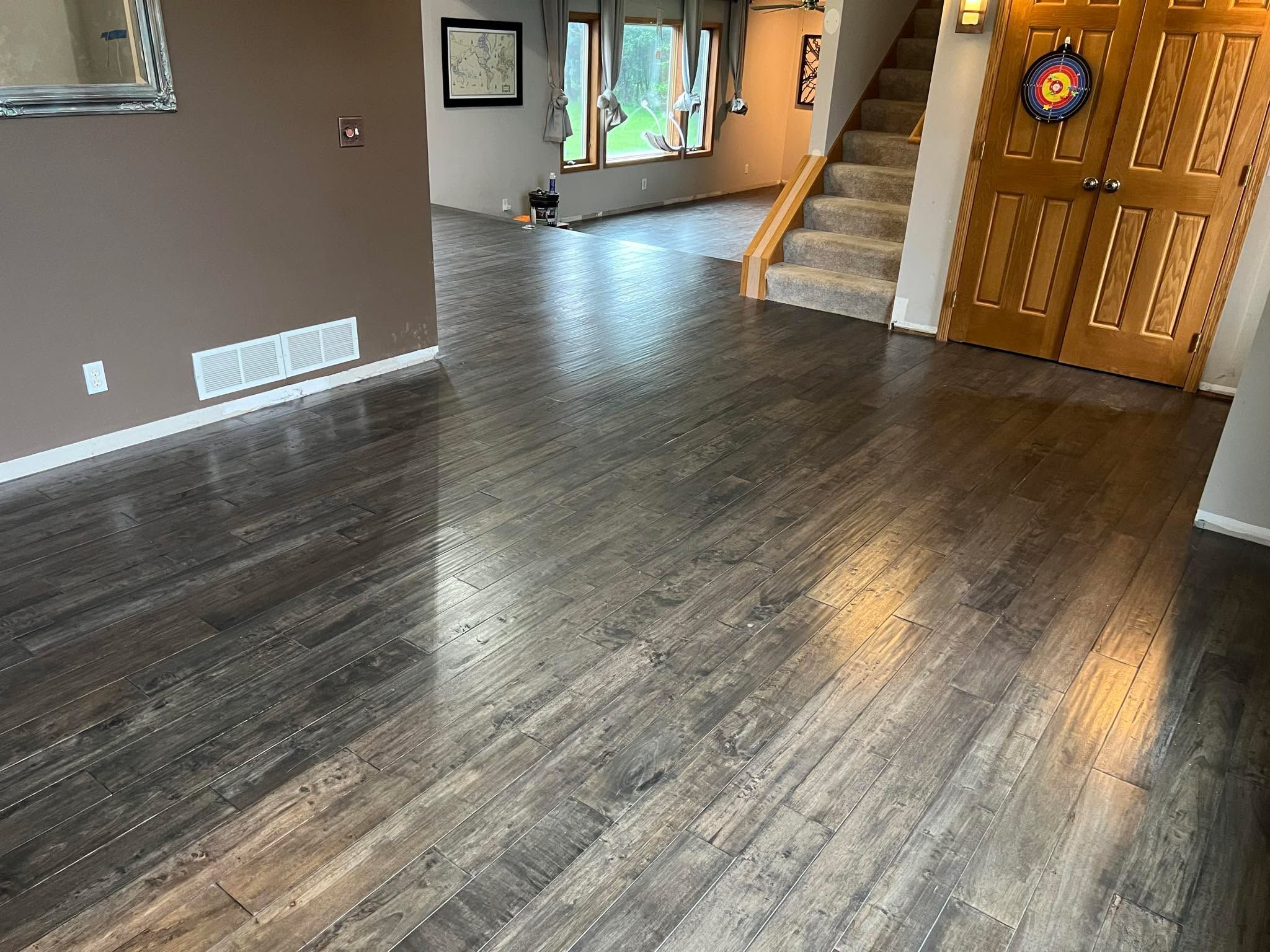Glued-down dark hardwood plank flooring in an entry and living room area with stairs and wooden doors visible.