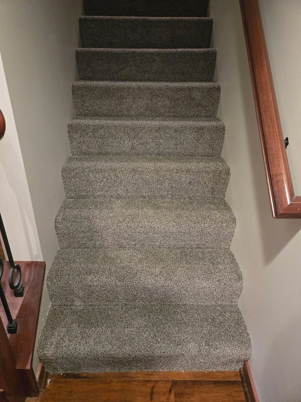 Gray textured carpet installed on staircase with wood handrail and white walls.