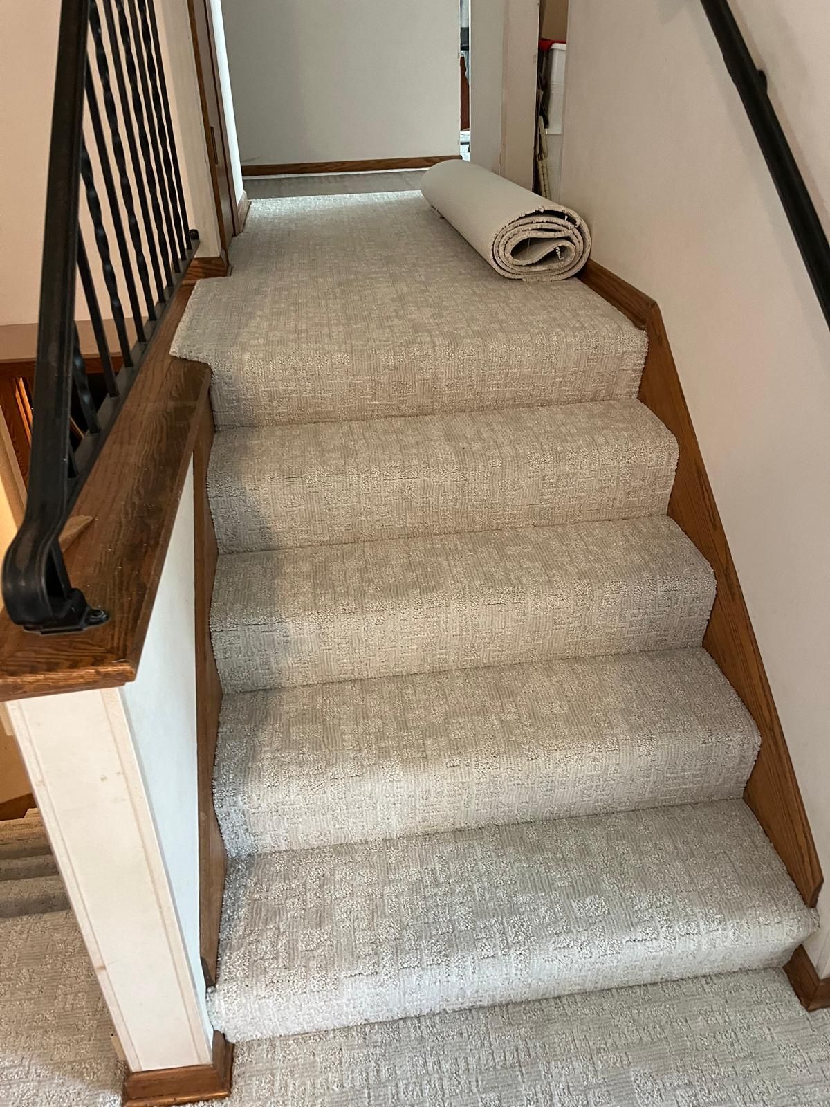 Beige carpet installed on staircase with wood stair nosing and rolled carpet on landing.