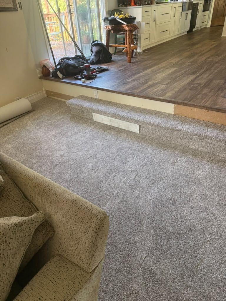 Gray carpet newly installed in a living room with transition strips visible between flooring materials.