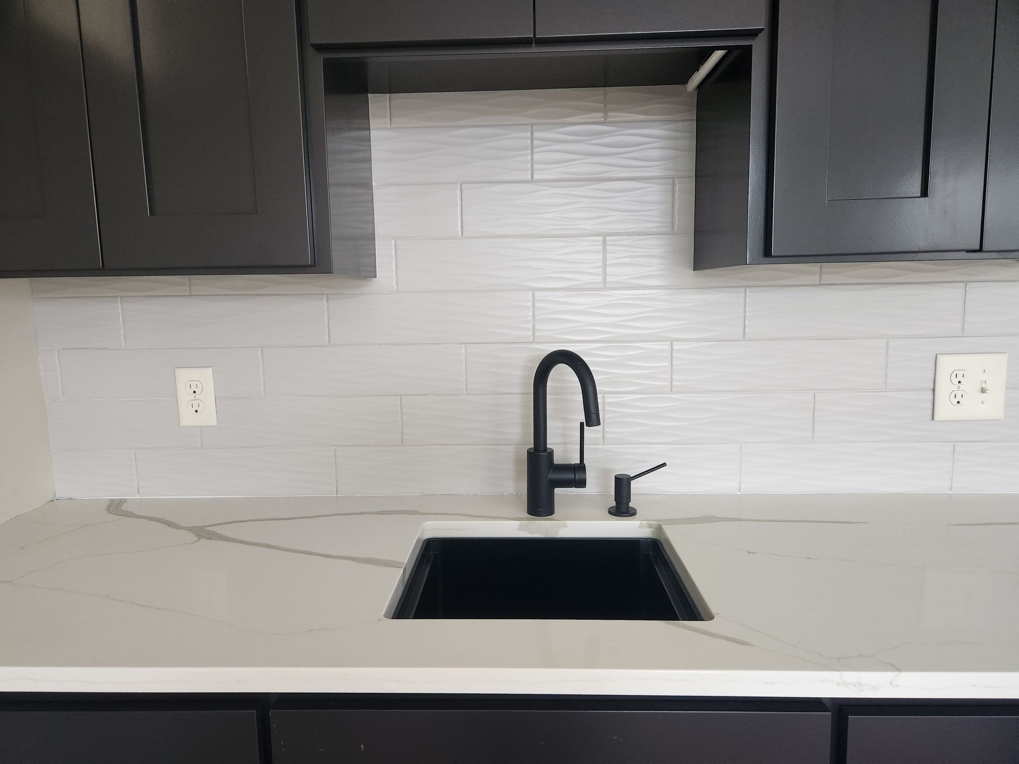 White subway tile backsplash installed above kitchen sink with black faucet and contemporary cabinets.