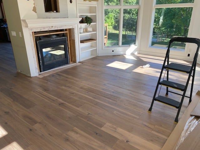 Medium-toned hardwood plank flooring in a living room with fireplace and white shelving.