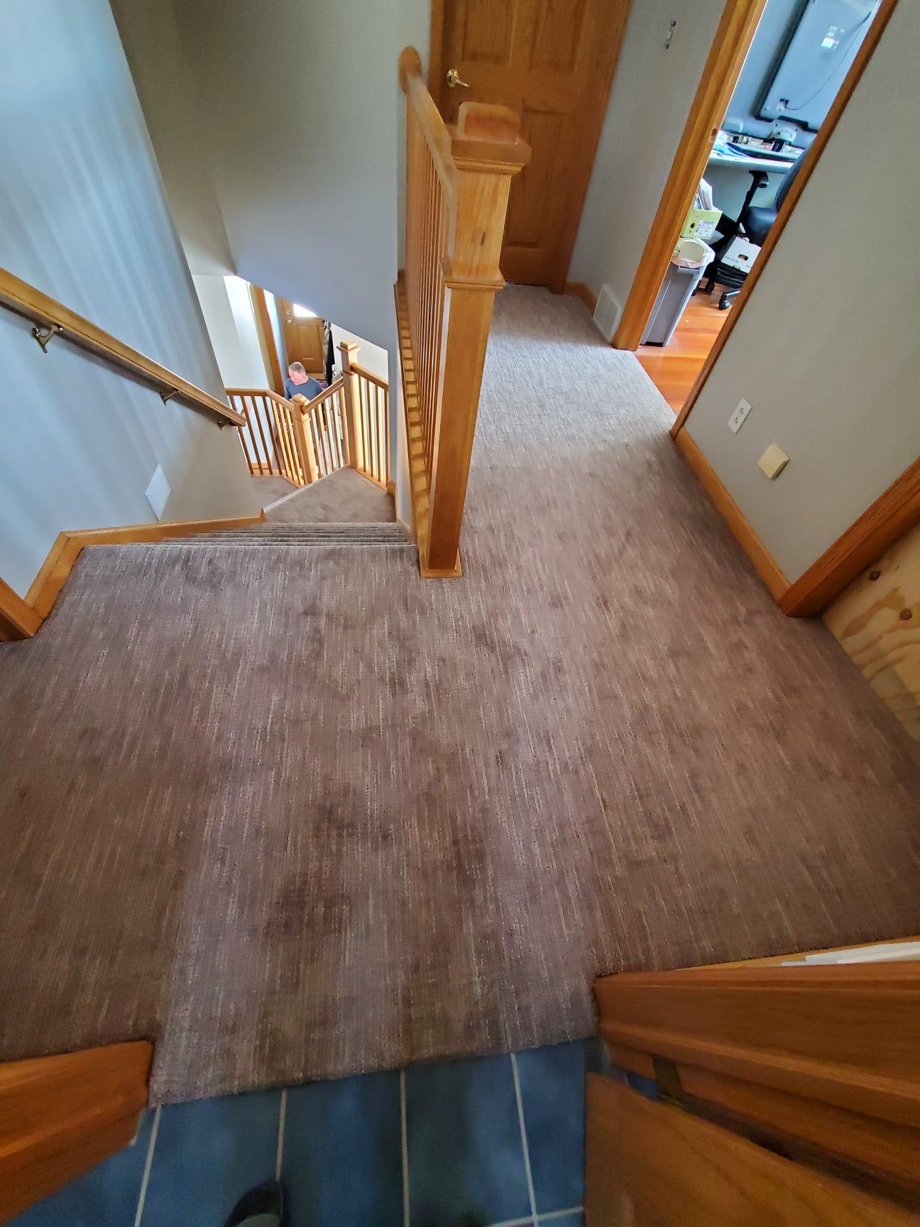 Hallway with new brown carpet installation adjacent to wooden stair railing and trim.