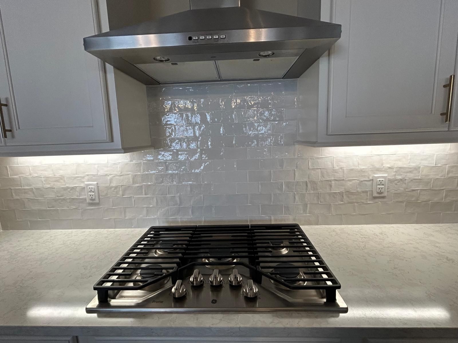 Kitchen with white subway tile backsplash behind a gas range with stainless steel hood.